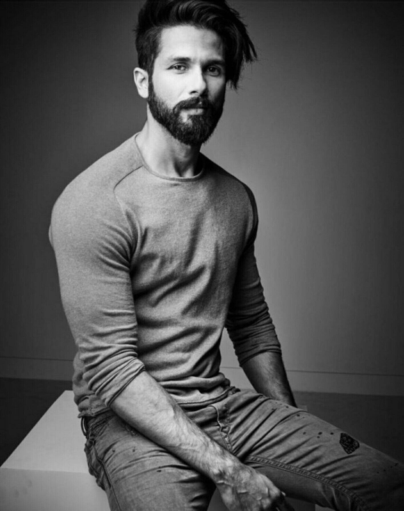 Shahid Kapoor 桌布 壁紙 — 一個留鬍子的男人穿著長袖襯衫，自信地坐在白色方塊上，背景是純灰色，營造出陰鬱的黑白肖像。