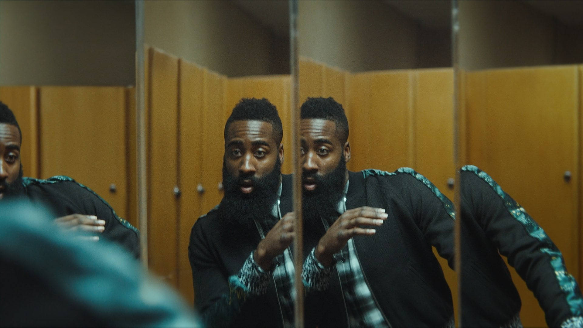 James Harden 桌布 壁紙 — 一個留鬍子的男人穿著黑色夾克，袖子有青綠色圖案，專注地盯著浴室鏡子中自己的倒影。