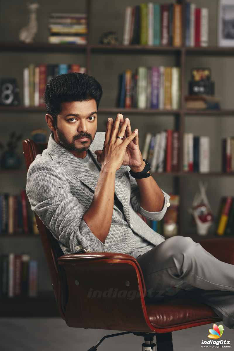 vijay HD 桌布 壁紙 — 一個留鬍子的男人自信地坐在紅色皮椅上，面前是裝滿書籍和裝飾品的書架。