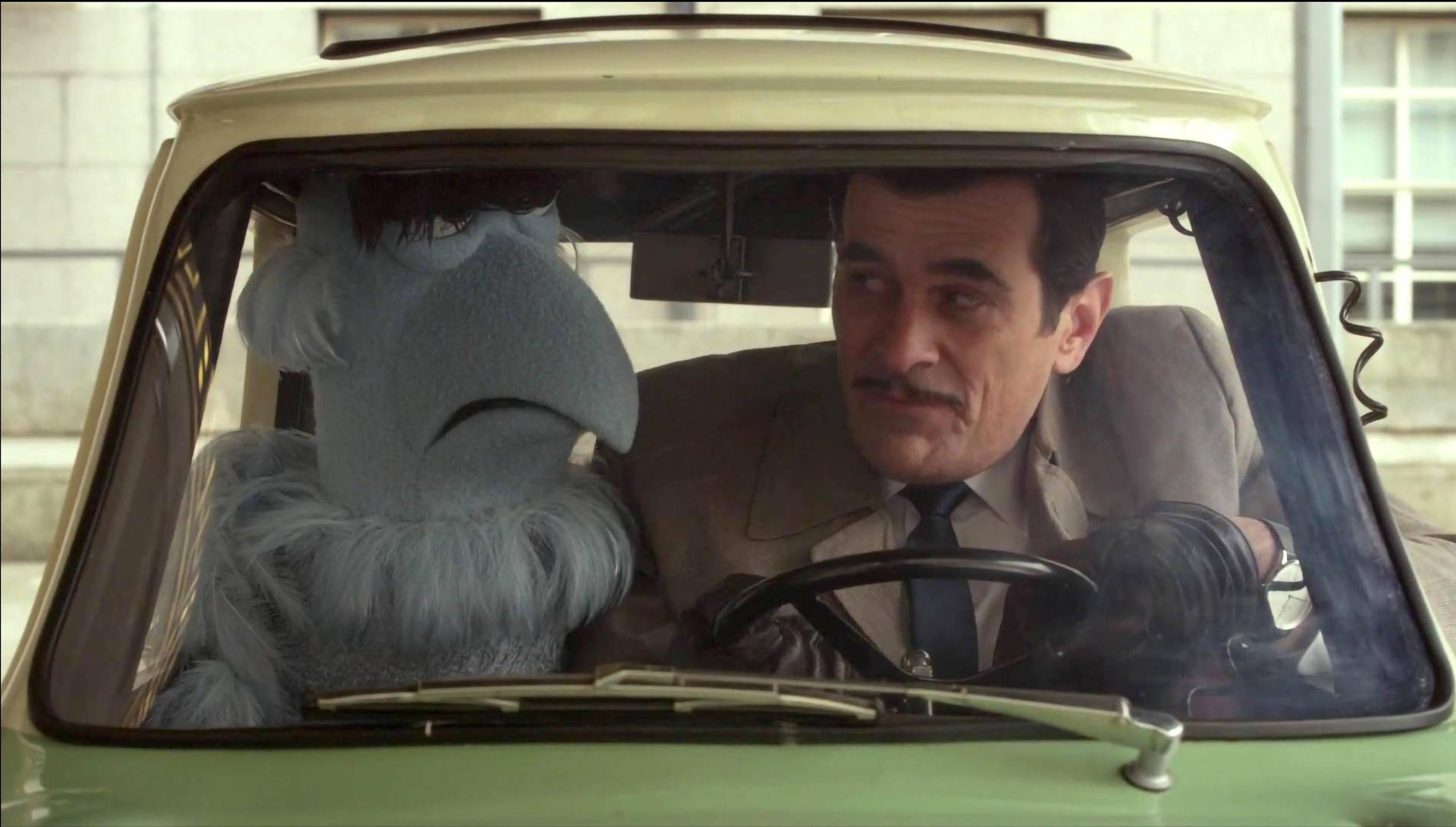 muppets 桌布 壁紙 — 一個留鬍子的男人駕駛一輛老爺車，而一個藍色毛絨公仔坐在他旁邊，看起來很傷心。