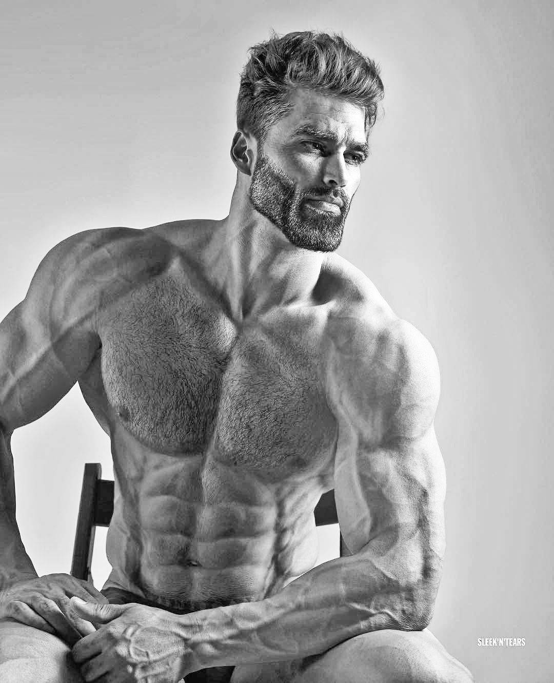 一個赤裸上身、留鬍子的肌肉男坐在工作室的椅子上。 — Giga Chad GIF 壁紙