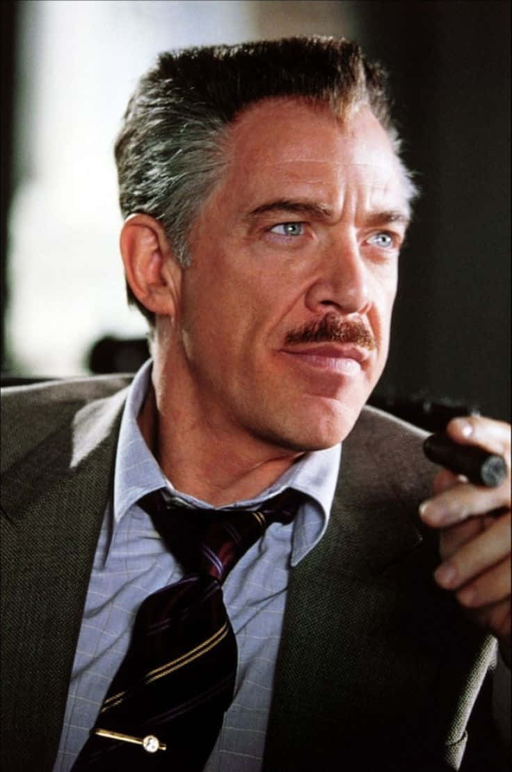 J Jonah Jameson 桌布 壁紙 — 一個留鬍子的西裝男子在昏暗的房間裡持槍，表情嚴肅。