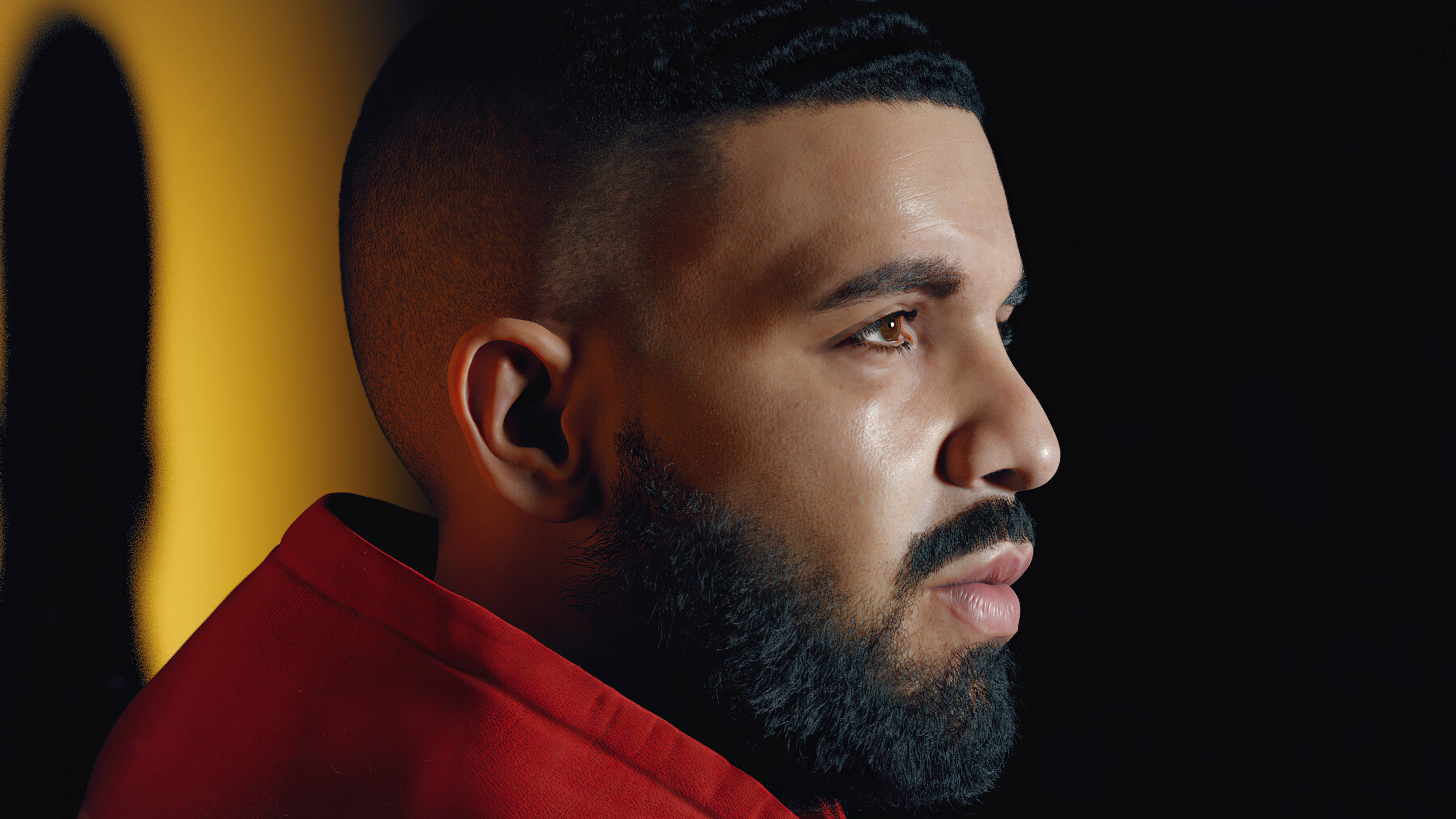 Drake 桌布 壁紙 — 一個留鬍子短髮的男人穿著紅色襯衫，在鮮明的黃色和黑色背景前若有所思地凝視。