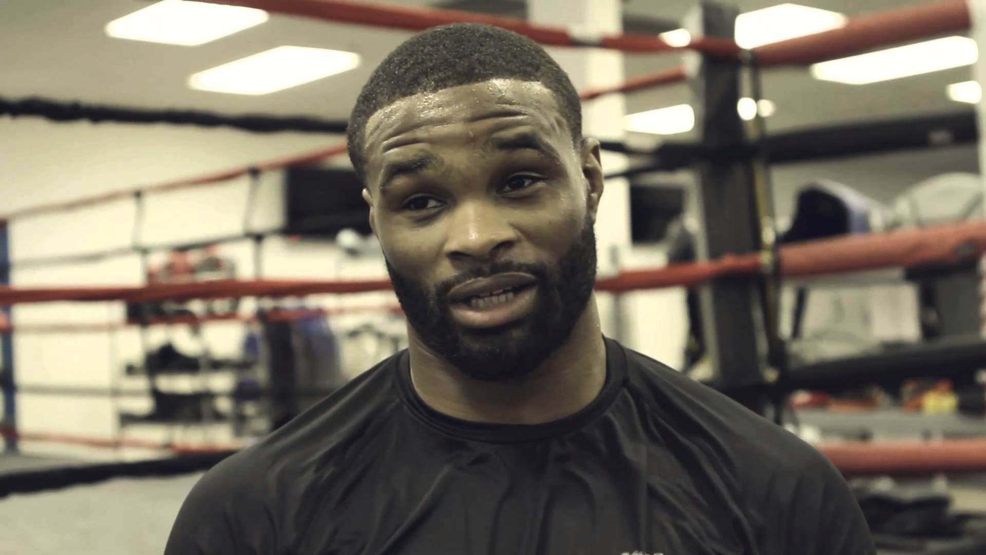 Tyron Woodley 桌布 壁紙 — 一個留鬍鬚、專注的拳擊手在明亮的頂燈下，在健身房的擂台上凝視著。