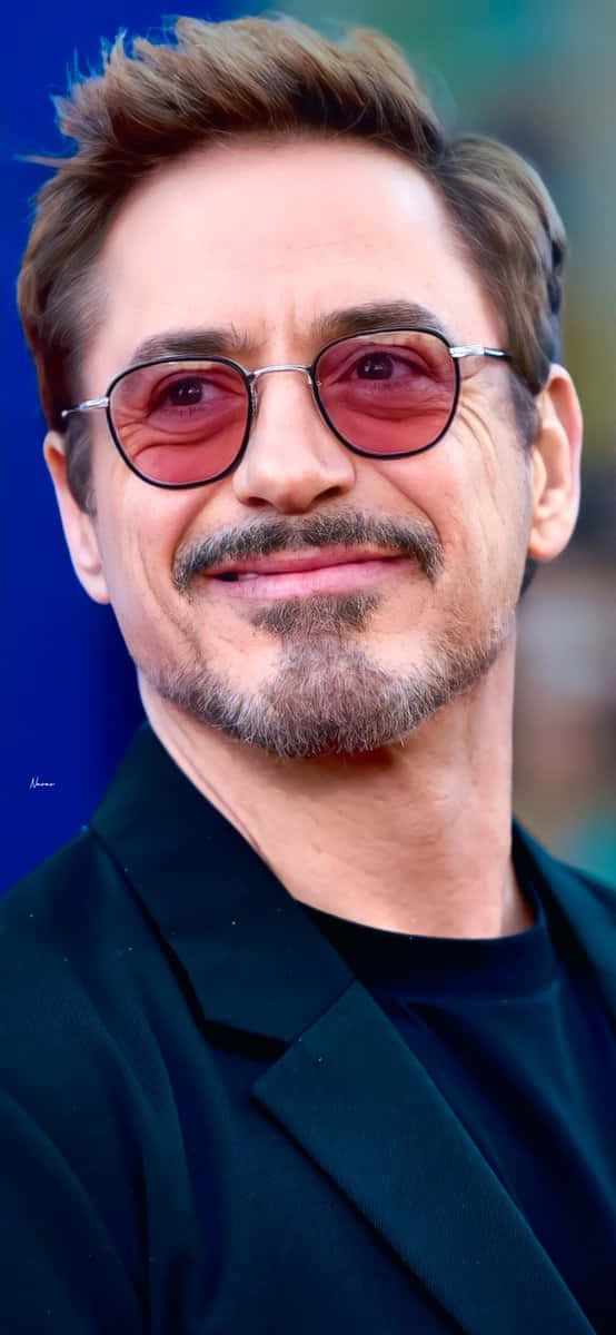 Hollywood 桌布 壁紙 — 一個留鬍鬚、戴圓形紅色眼鏡的男人在藍色背景前微笑的特寫肖像。