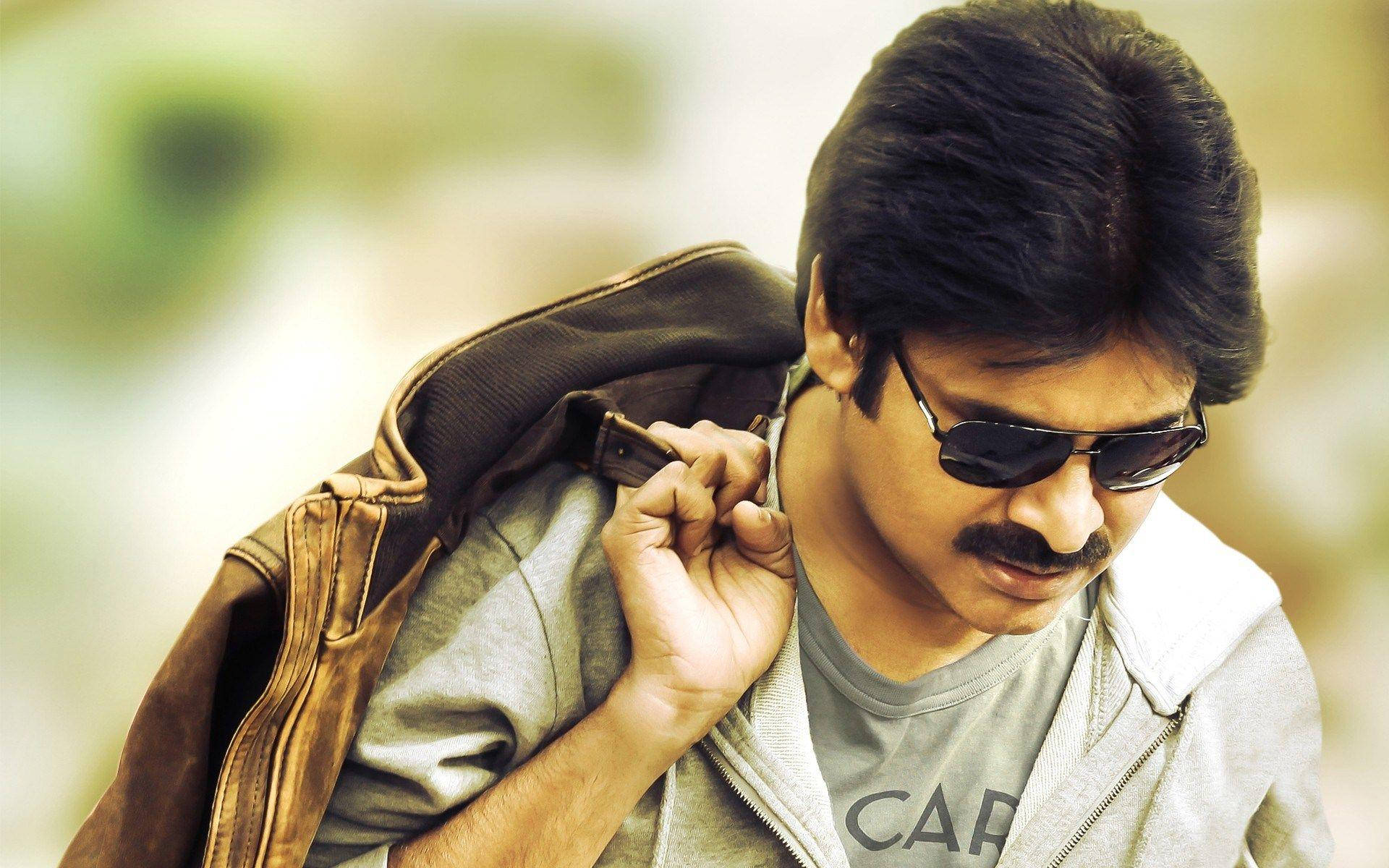 Pawan Kalyan 桌布 壁紙 — 一個留鬍鬚、戴太陽眼鏡的男人，在柔和模糊的背景前，將一件棕色外套搭在肩上。