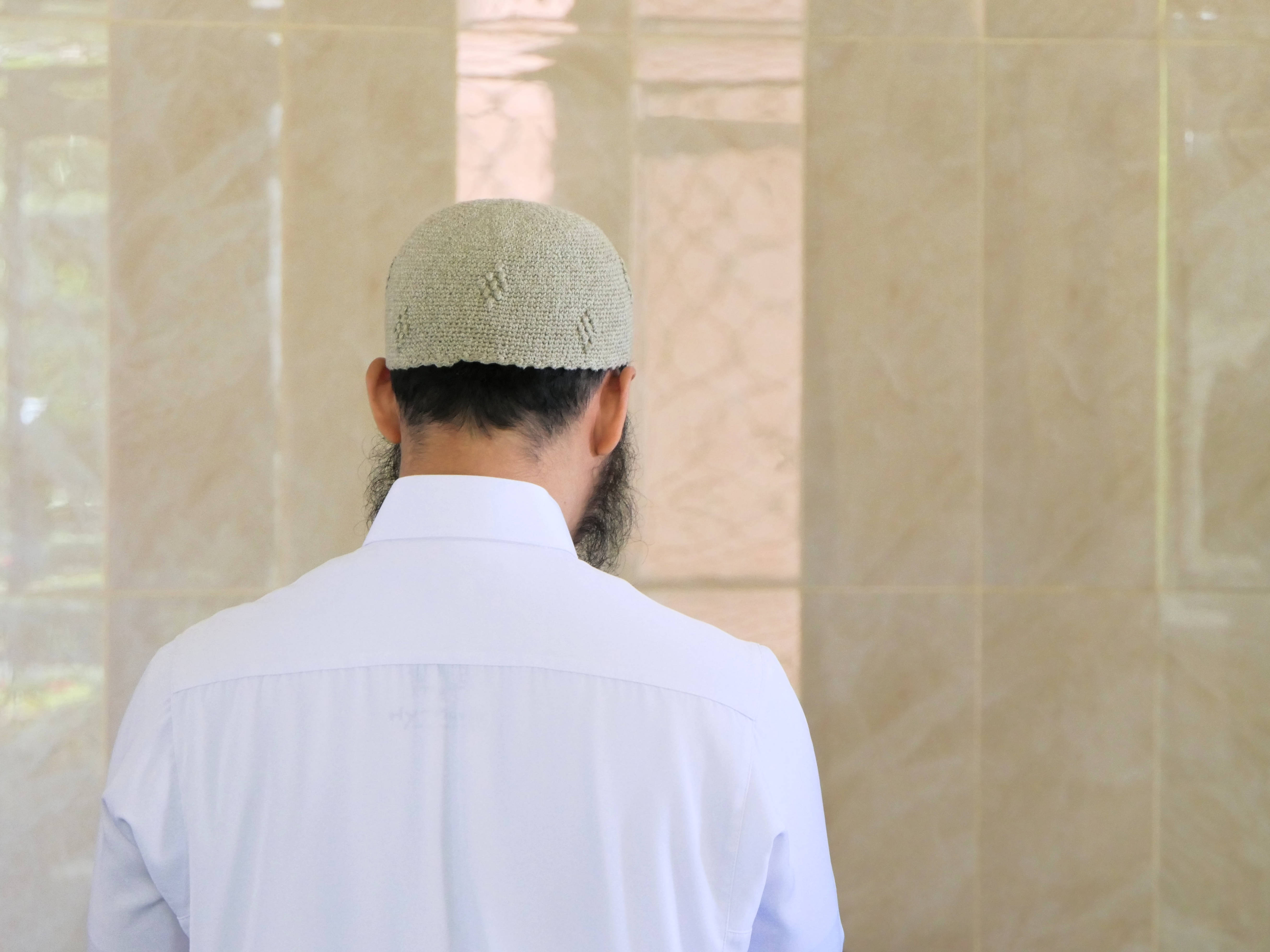 muslim 桌布 壁紙 — 一個留鬍鬚、戴淺綠色針織帽的男人背對鏡頭，站在米色瓷磚牆前。