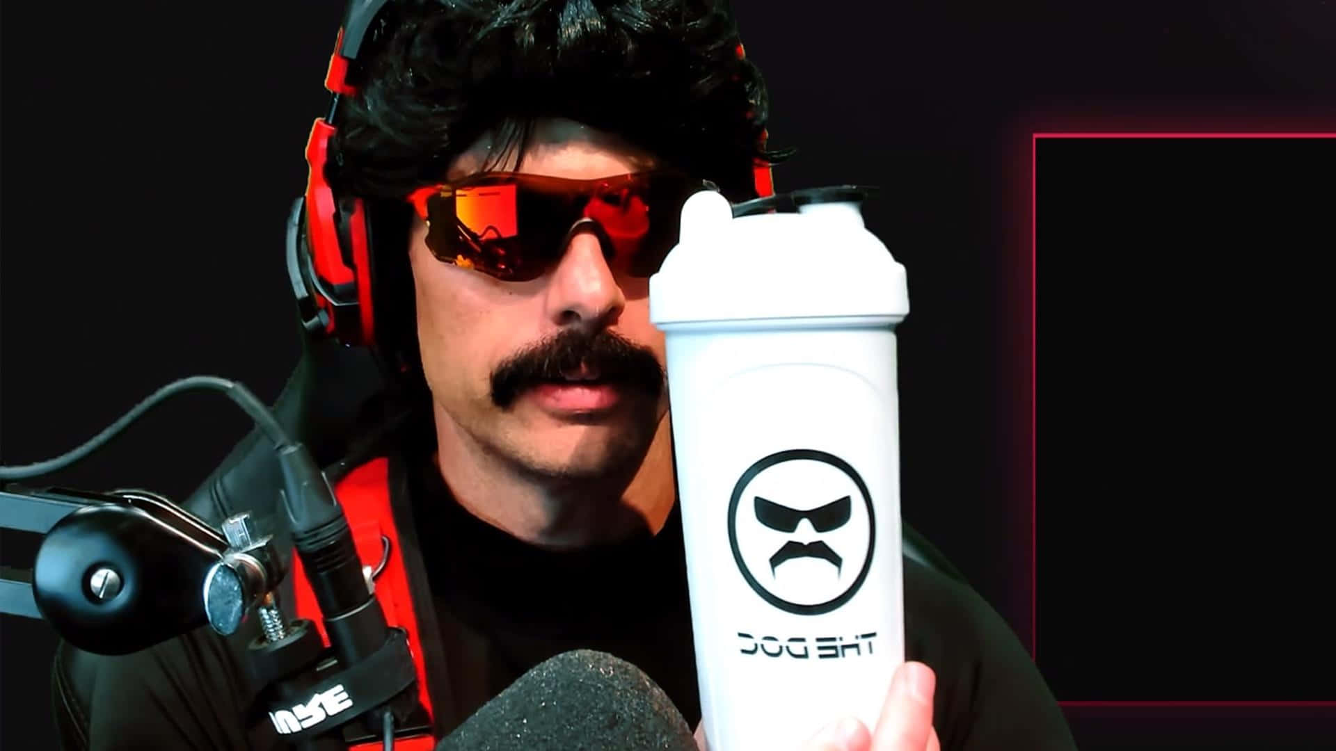 Dr Disrespect 桌布 壁紙 — 一個留鬍鬚、戴紅色太陽眼鏡的男人，在帶有霓虹燈裝飾的黑暗工作室中，戴著紅色耳機，手持一個印有 'THE DOC' 標誌的白色搖搖杯。