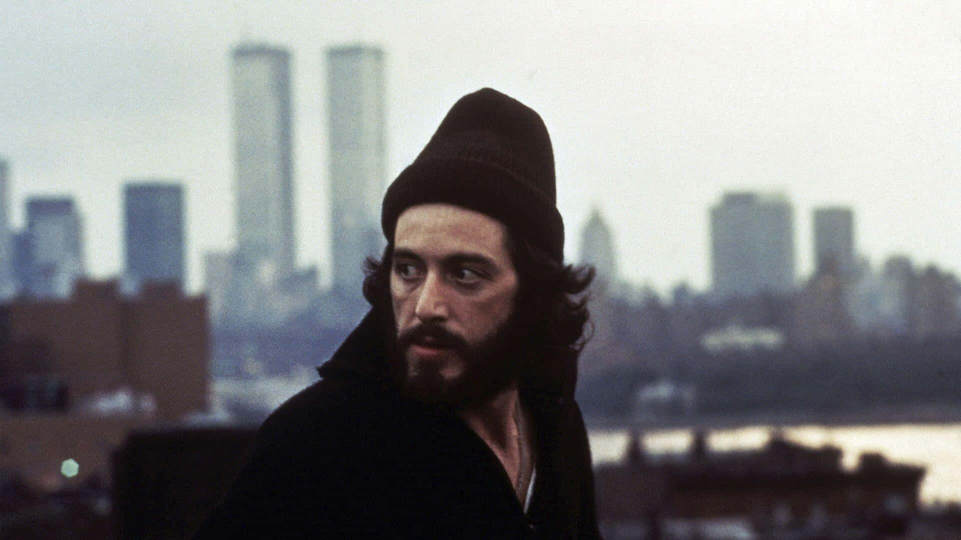 Al Pacino 桌布 壁紙 — 一個留鬍鬚、戴黑色毛帽的男人，專注地凝視著遠方可見雙子塔的朦朧紐約天際線。