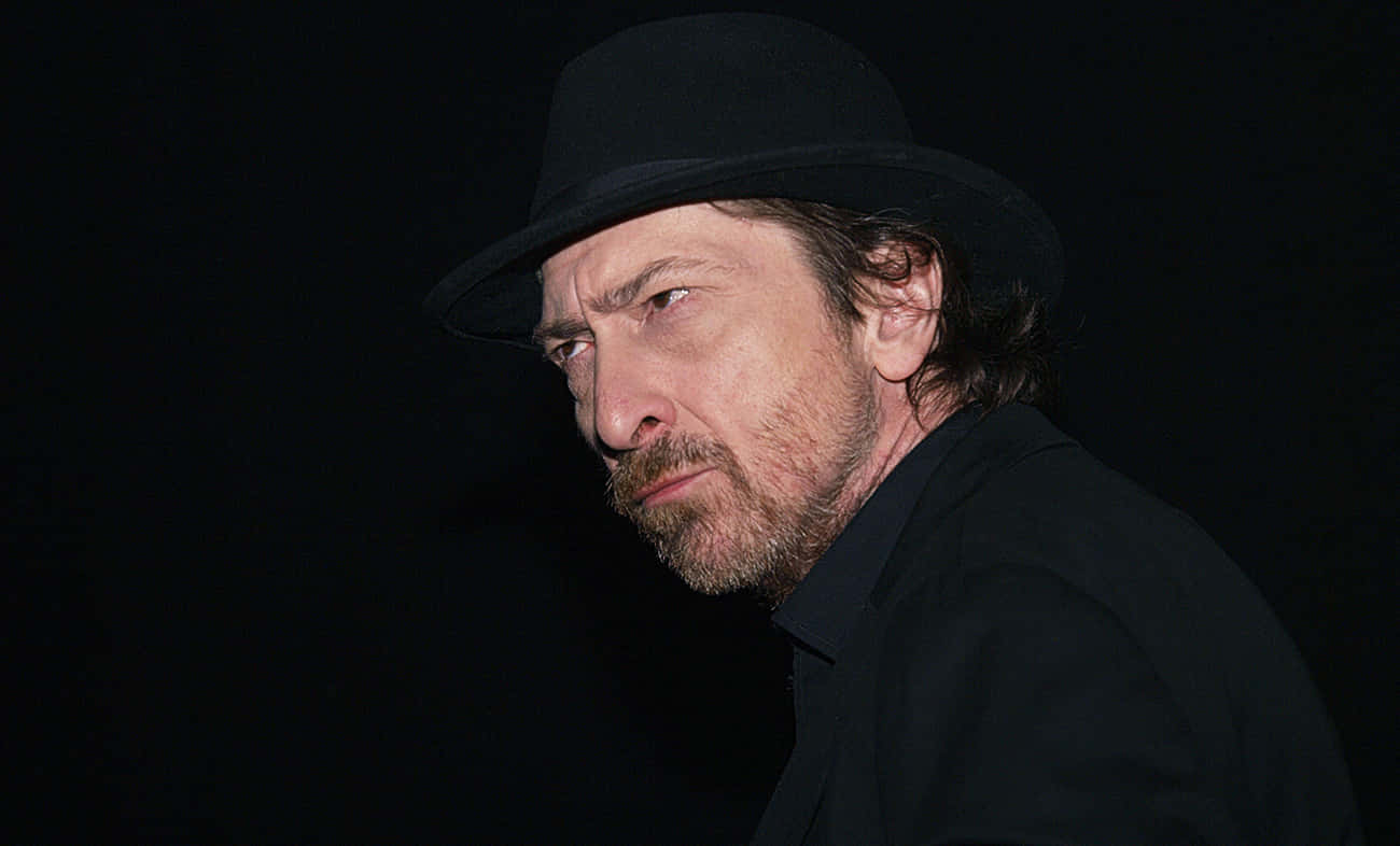 Frank Miller 桌布 壁紙 — 一個留鬍鬚、戴黑色軟呢帽的男人，在戲劇性燈光下，對著黑暗背景專注地凝視。