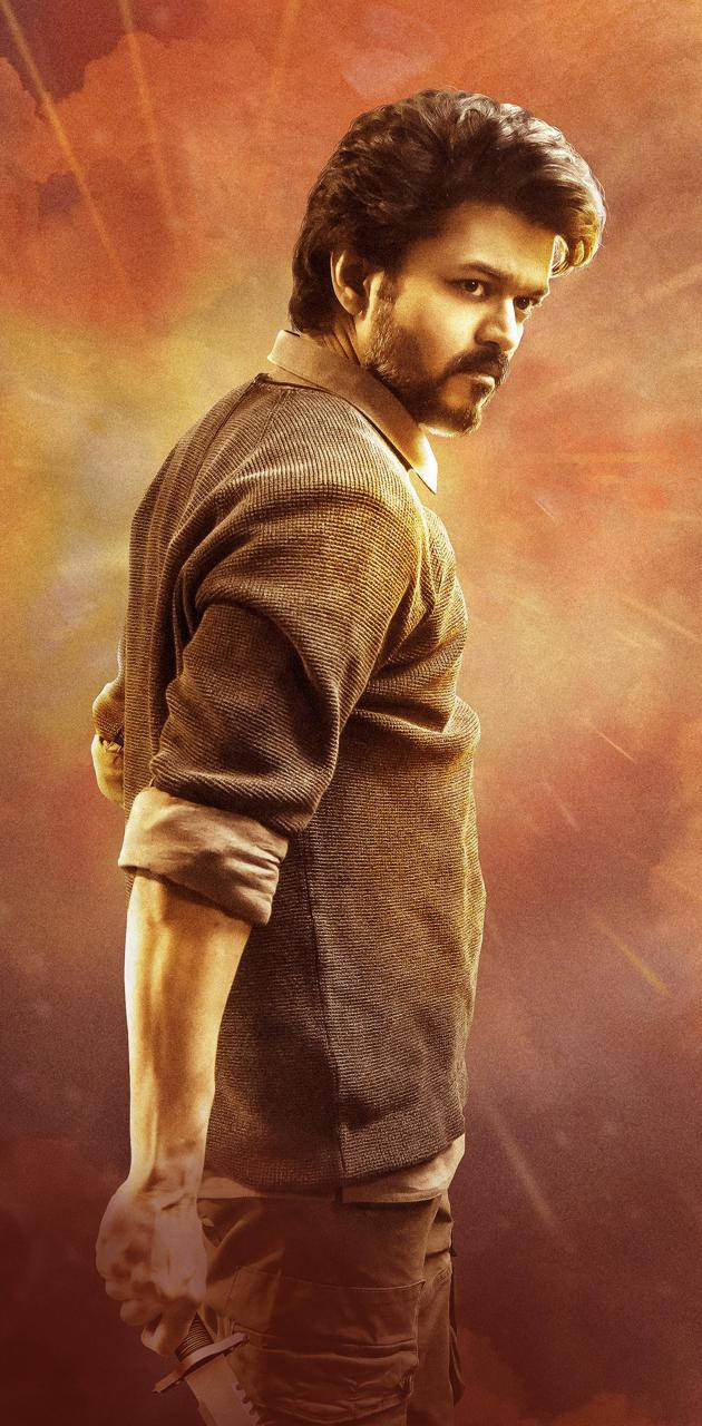 Bollywood HD 桌布 壁紙 — 一個留鬍鬚、眼神專注的男人站在熾熱的橙紅色光芒中，穿著一件有紋理的棕色毛衣。