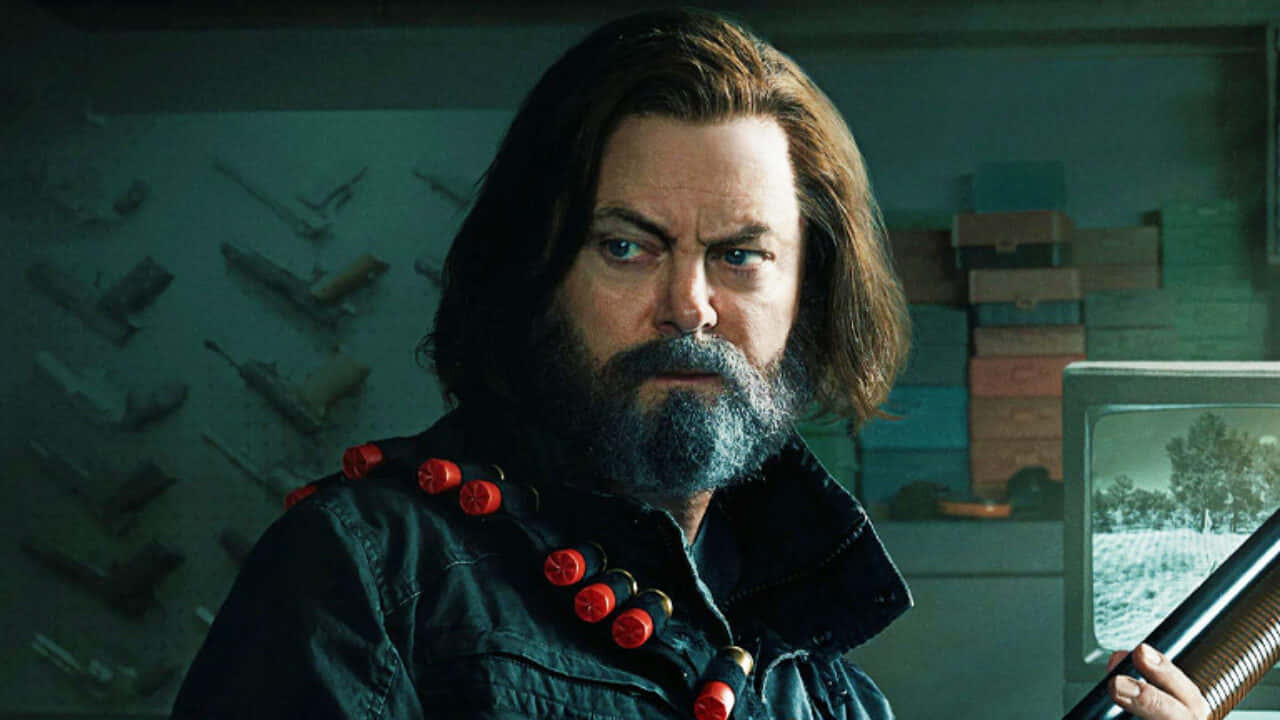 nick offerman 桌布 壁紙 — 一個留鬍鬚、眼神銳利的男人，在一個昏暗的房間裡拿著一把獵槍，房間裡有一台復古電視和堆疊的箱子。