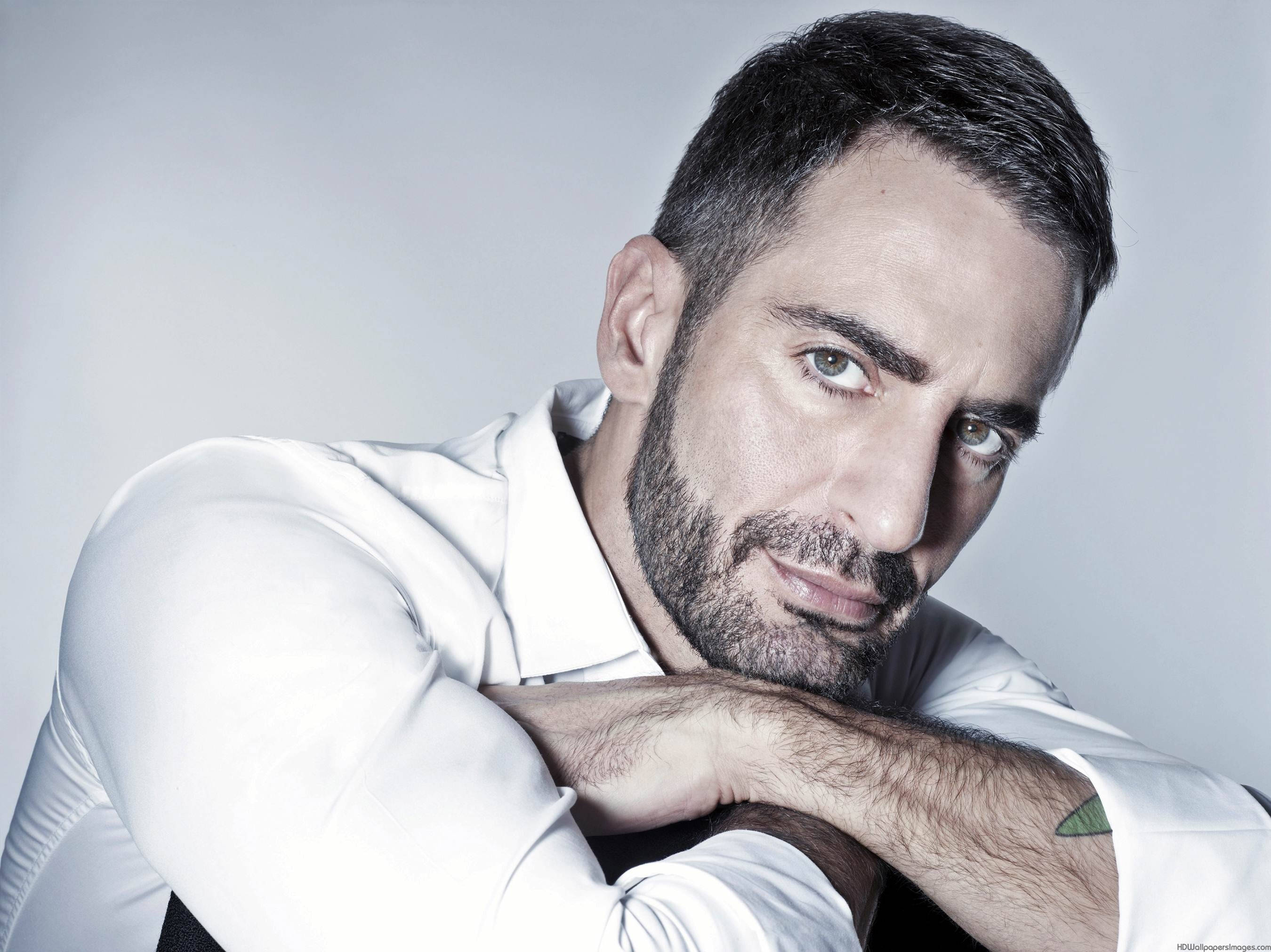 Marc Jacobs 桌布 壁紙 — 一個留鬍鬚、眼神銳利的男人，將下巴擱在手臂上，背景是純灰色，身穿一件挺括的白襯衫。