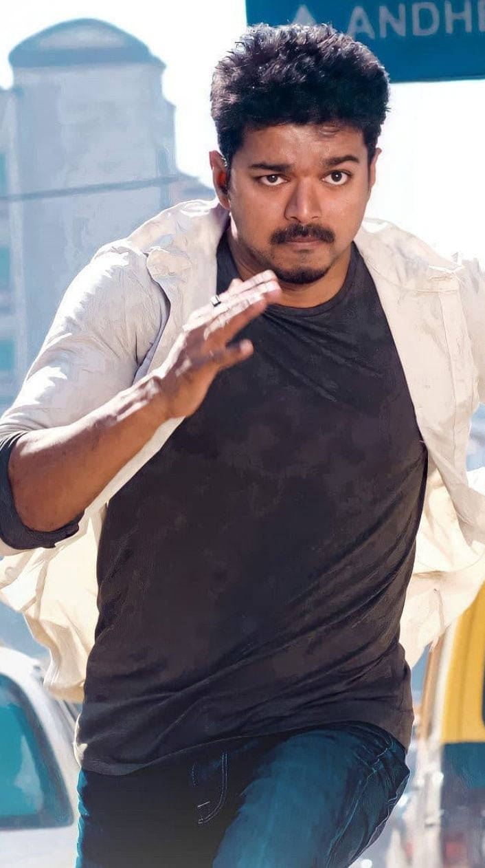 vijay HD 桌布 壁紙 — 一個留鬍鬚、眼神銳利的男人，穿著黑色襯衫和敞開的白色外套，在城市街道上向前奔跑。