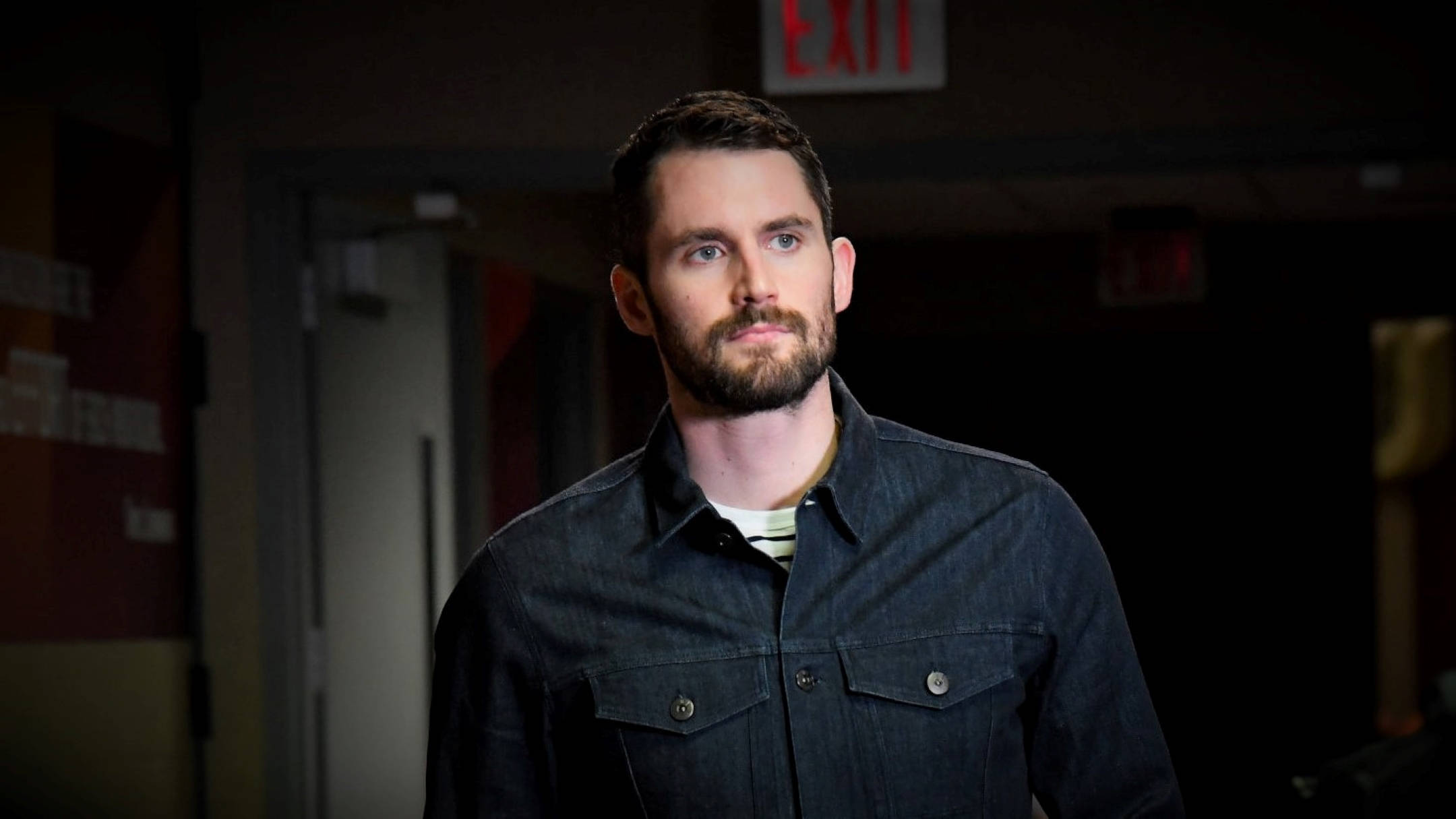 Kevin Love 桌布 壁紙 — 一個留鬍鬚、穿深色襯衫的男人站在昏暗的走廊裡，上方有出口標誌。