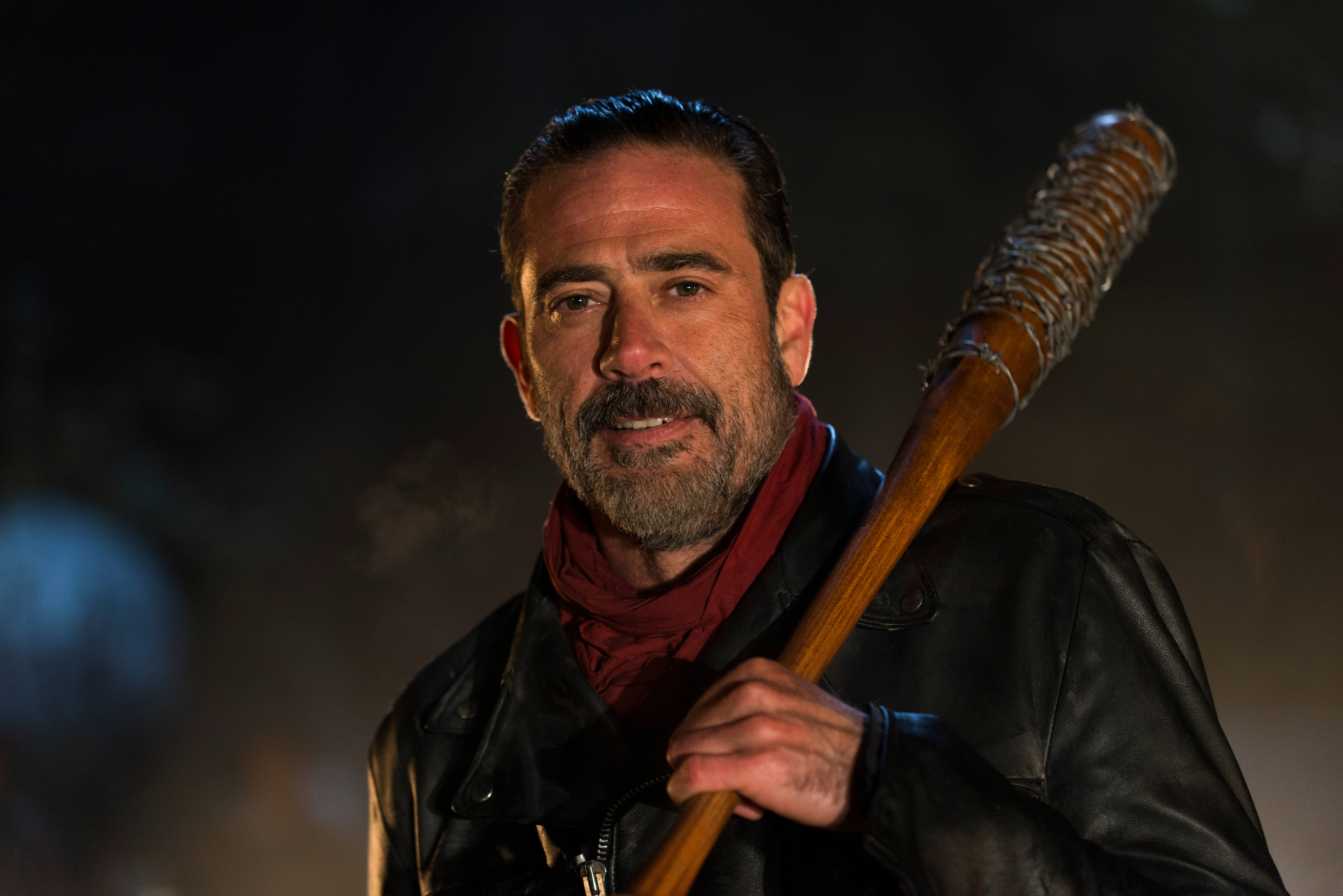 Negan 桌布 壁紙 — 一個留鬍鬚、穿皮夾克的男人在昏暗的夜燈下，背景有煙霧，手持一支帶釘的球棒。