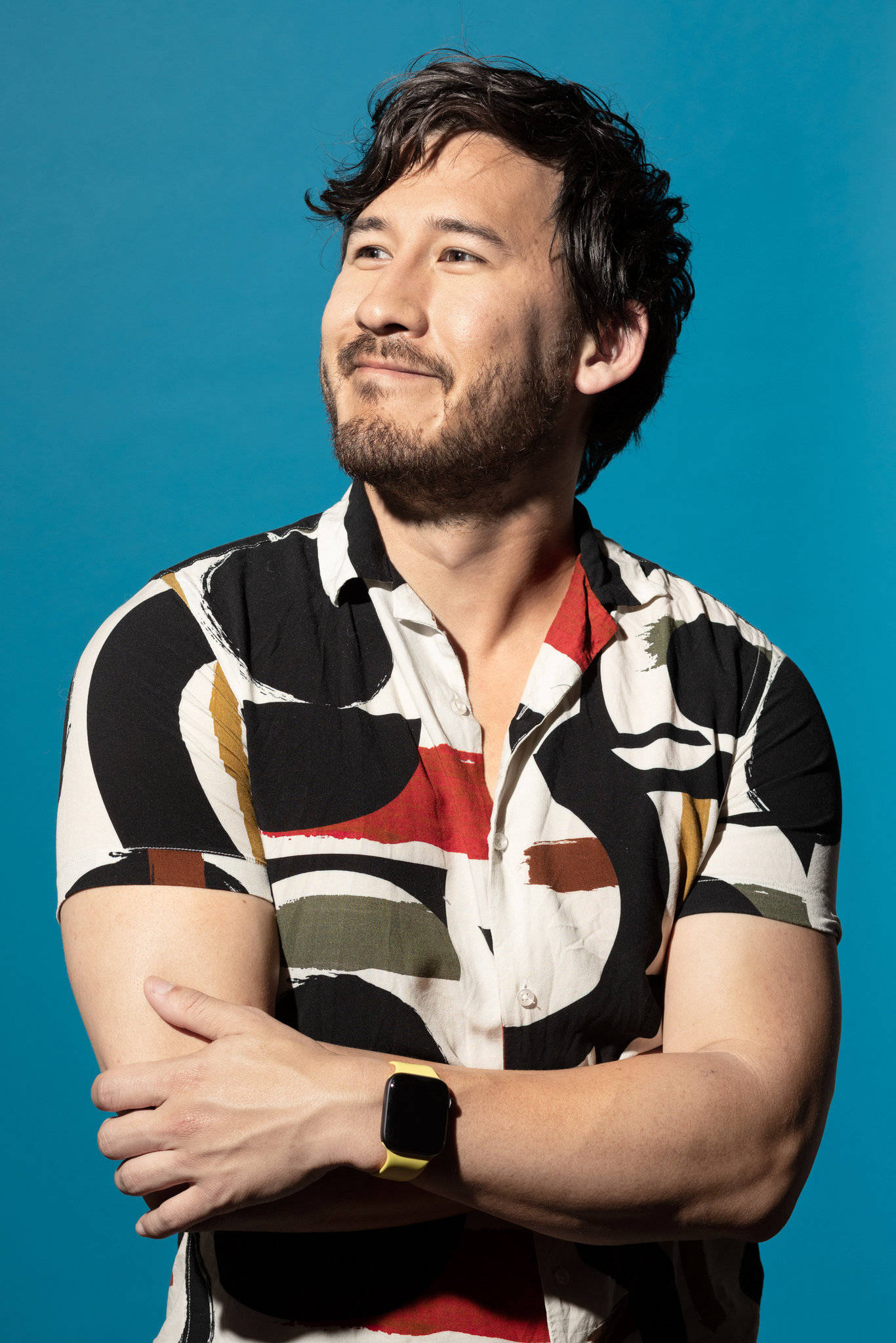 Markiplier 桌布 壁紙 — 一個留鬍鬚、穿著圖案襯衫的男人自信地交叉雙臂站在純藍色背景前。