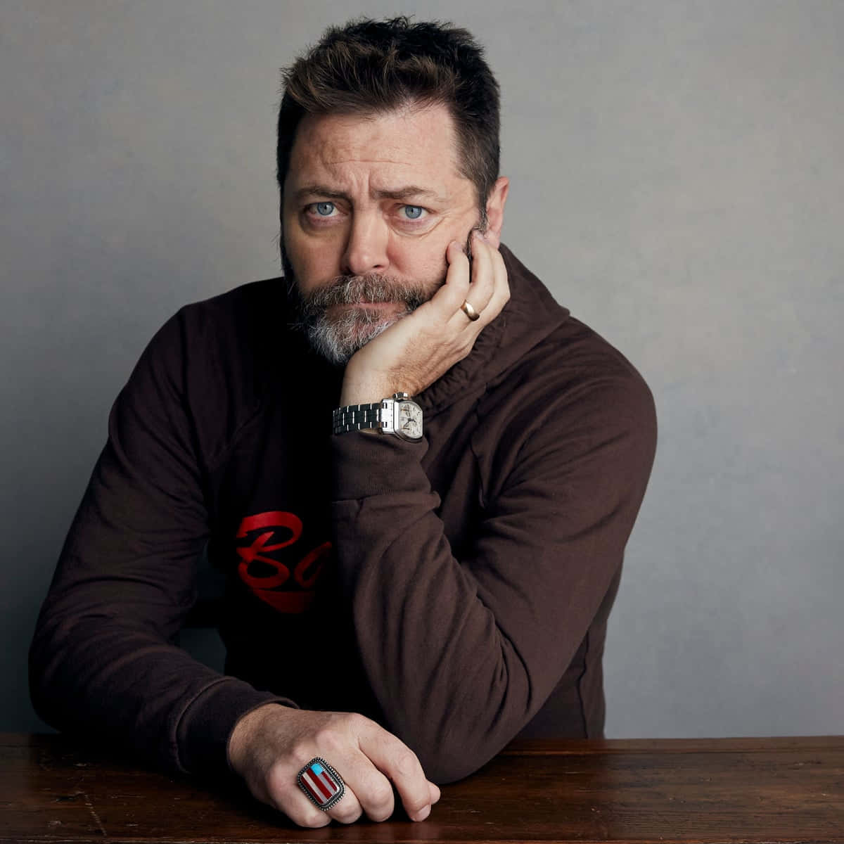 nick offerman 桌布 壁紙 — 一個留鬍鬚、藍眼睛的男人，將下巴擱在手上，穿著棕色連帽衫和一個獨特的戒指。