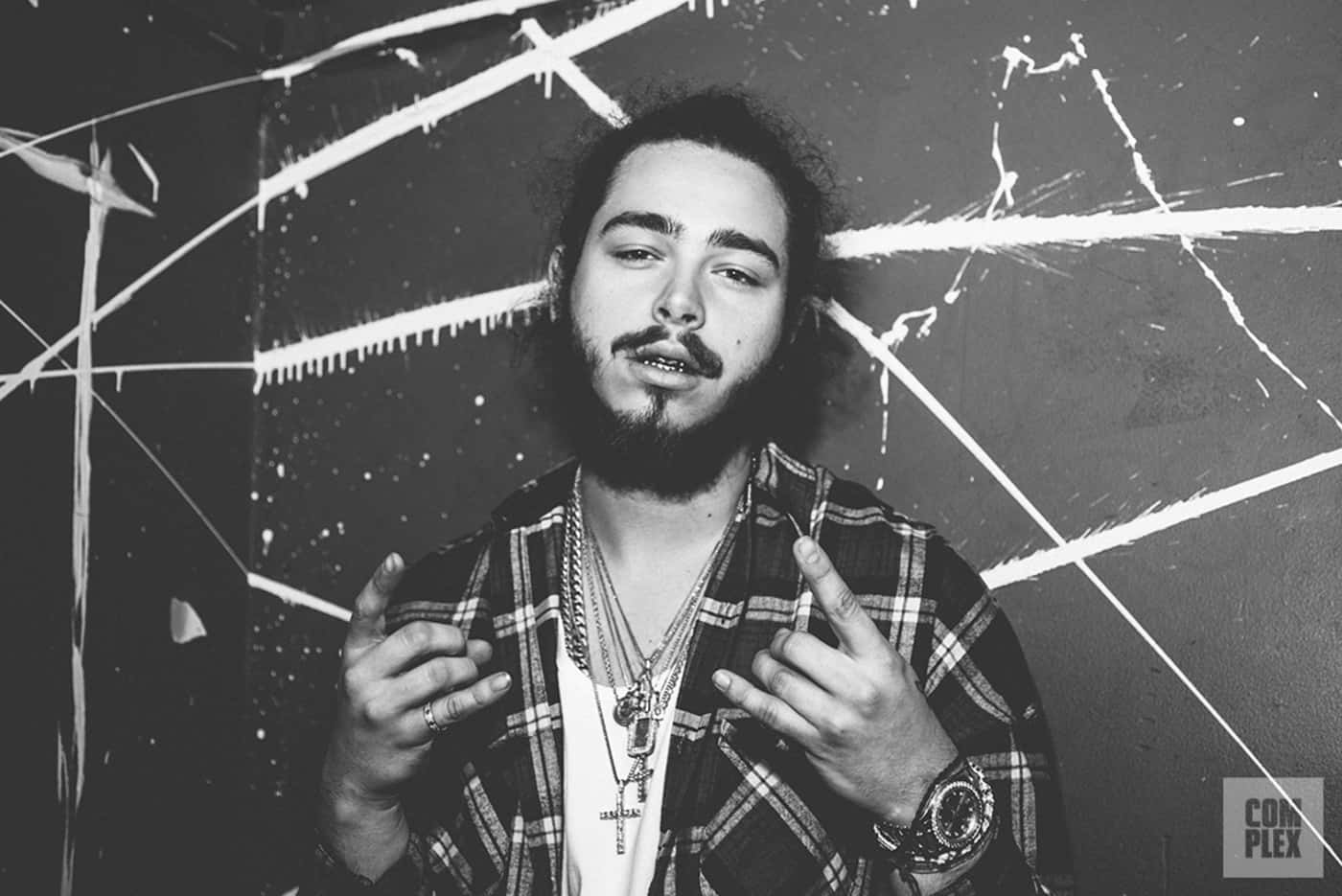 波斯特·马龙 桌布 壁紙 — 一個留鬍鬚、身穿格子襯衫的男人，在一個佈滿塗鴉的牆前做手勢，這是一幅粗獷的黑白肖像。