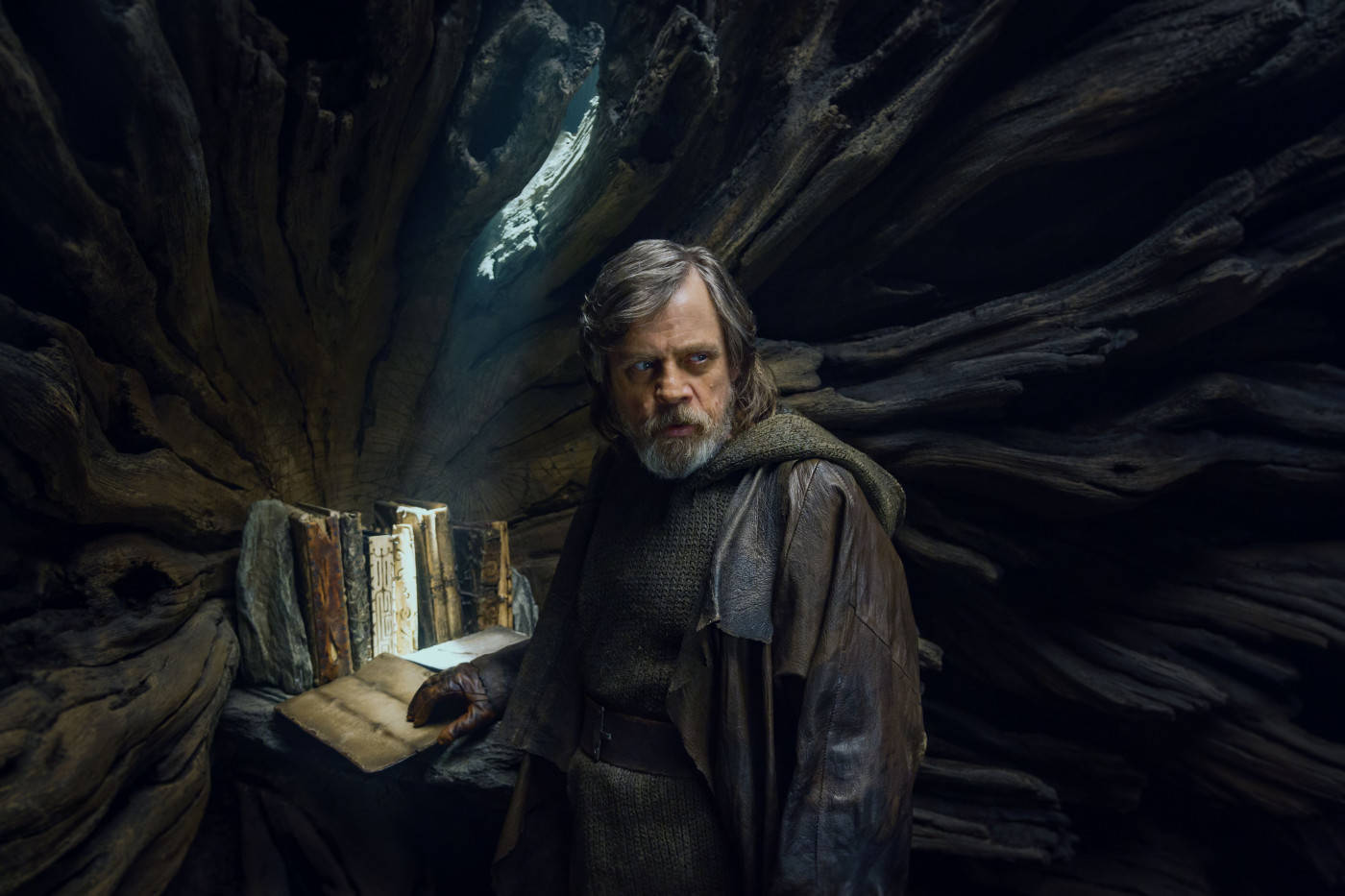 Star Wars Landscape 桌布 壁紙 — 一個留鬍鬚、身穿長袍的男人莊嚴地站在黑暗的樹根洞穴中，手持一本打開的書，光線從上方傾瀉而下。