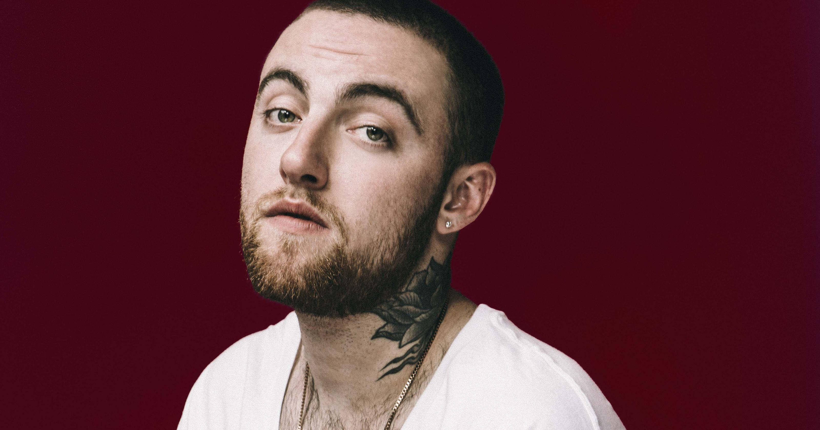 Mac Miller 桌布 壁紙 — 一個留鬍鬚、頸上有刺青的男人，在深紅色工作室背景前凝視著。