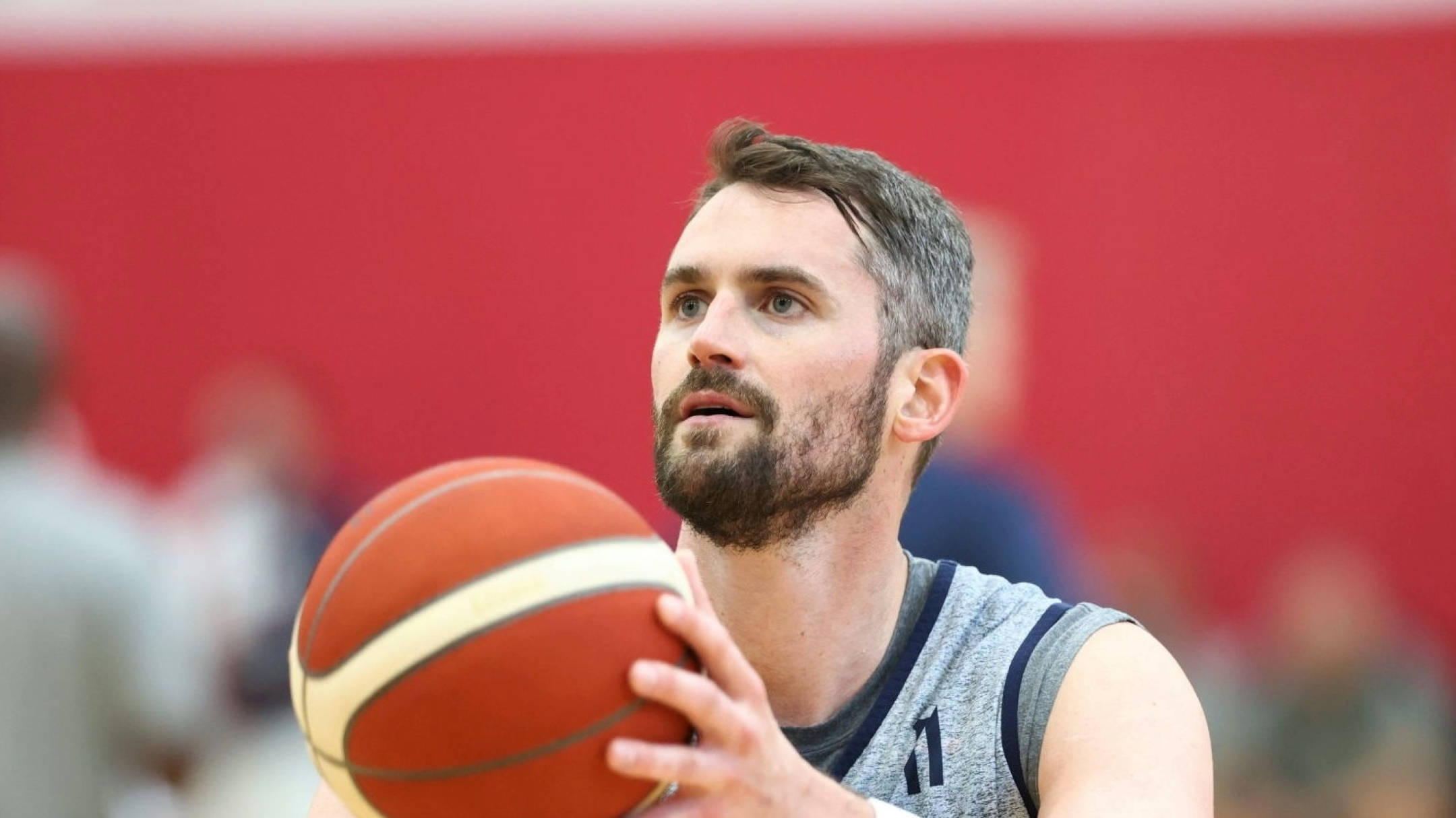 Kevin Love 桌布 壁紙 — 一個留鬍鬚的專注籃球運動員，在紅色健身室牆前投籃中途拿著球。