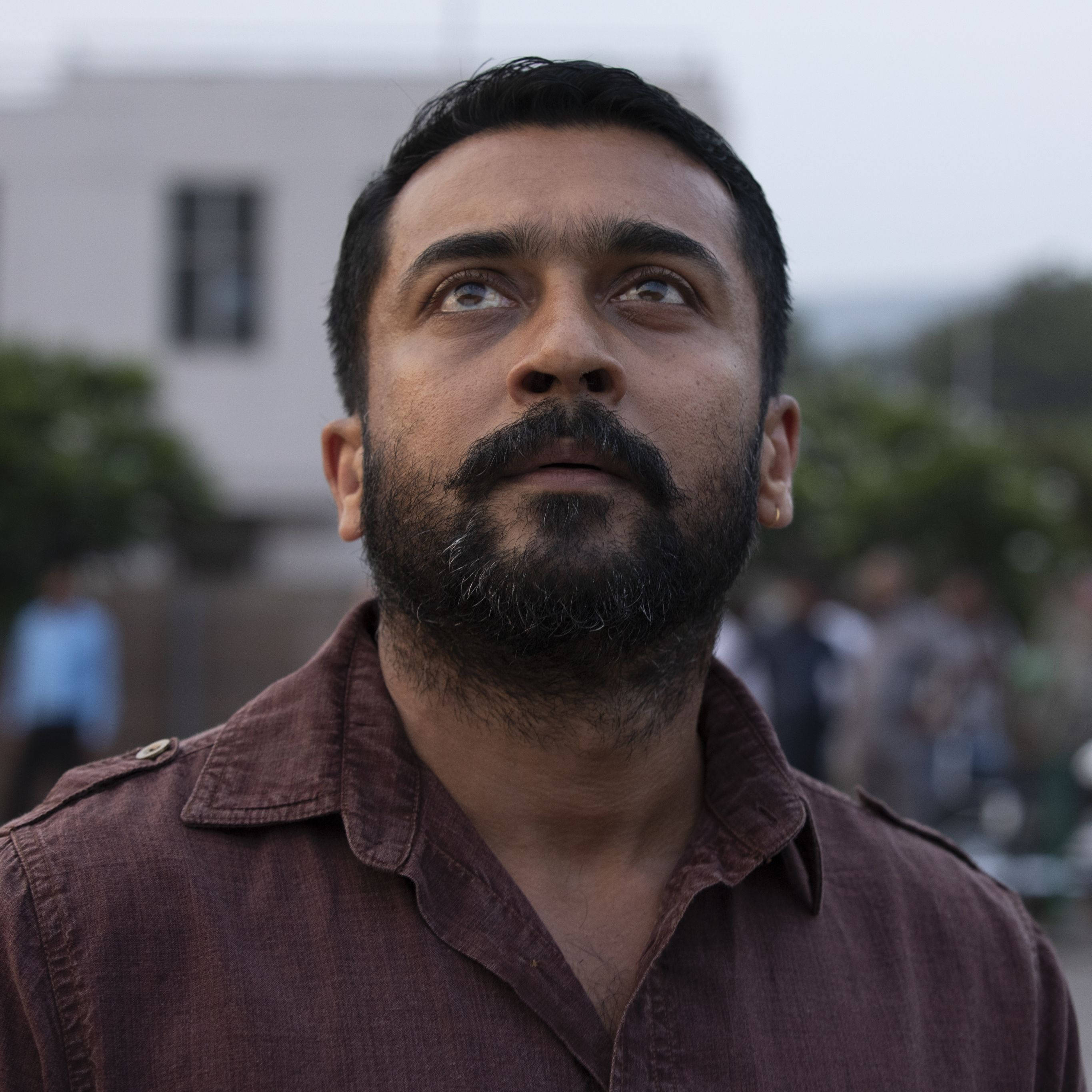 Indian 桌布 壁紙 — 一個留鬍鬚的男人，在模糊的城市背景下，帶著沉思的表情向上凝視。