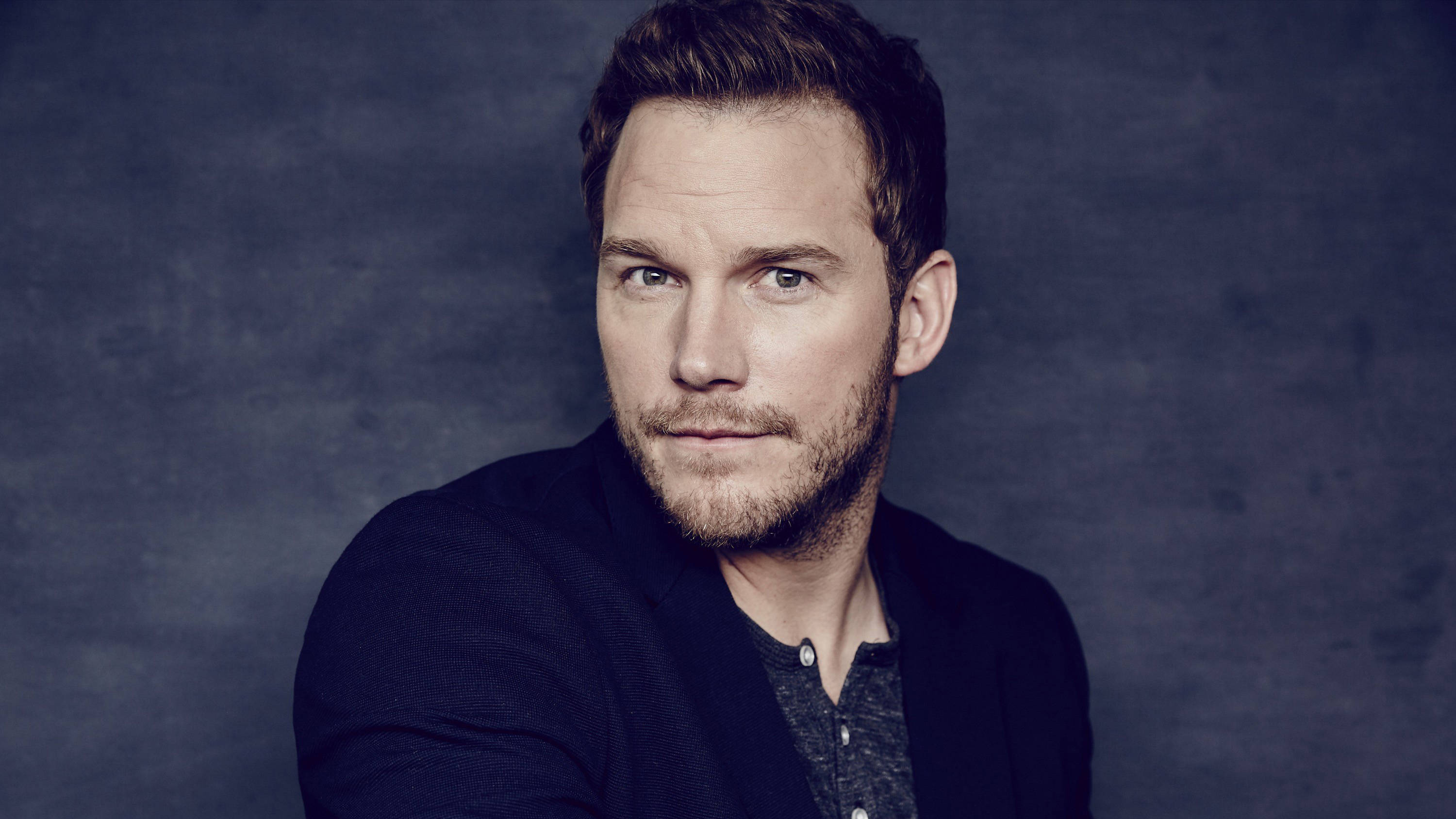 Chris Pratt 桌布 壁紙 — 一個留鬍鬚的男人，目光銳利，直視鏡頭，背景是帶有紋理的深藍色攝影棚。