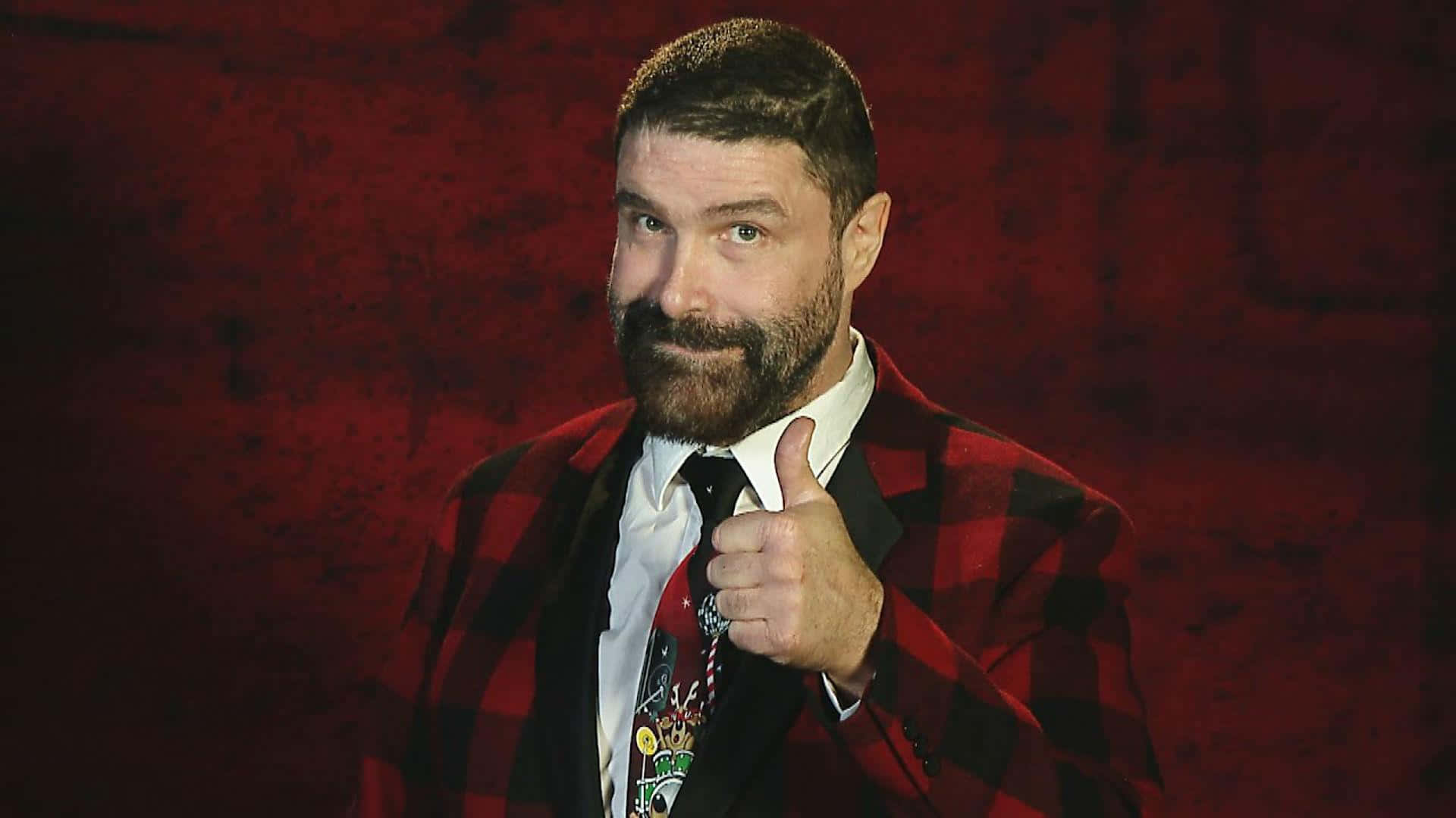 WWE 桌布 壁紙 — 一個留鬍鬚的男人，穿著紅色格子外套，在紋理紅色背景前豎起大拇指。