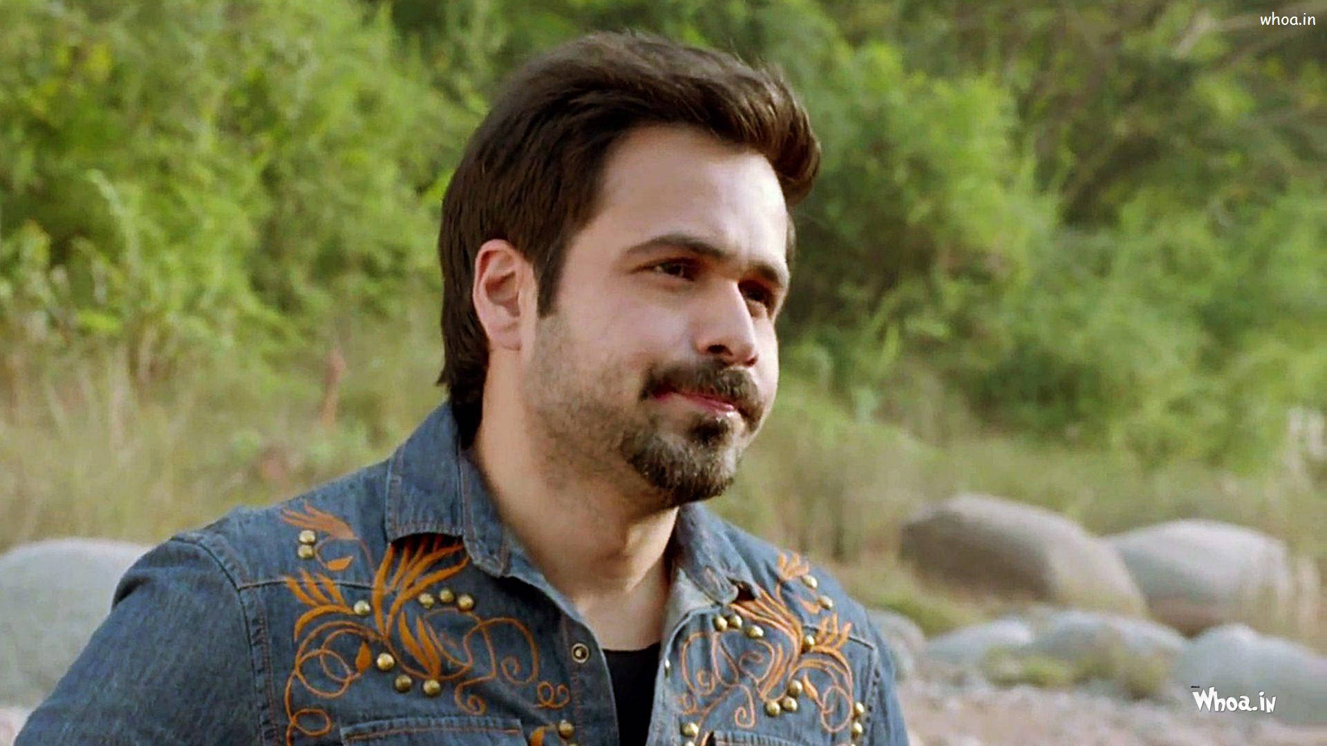 Emraan Hashmi 桌布 壁紙 — 一個留鬍鬚的男人，穿著裝飾性的牛仔外套，在陽光普照的綠色森林裡的岩石旁邊沉思。