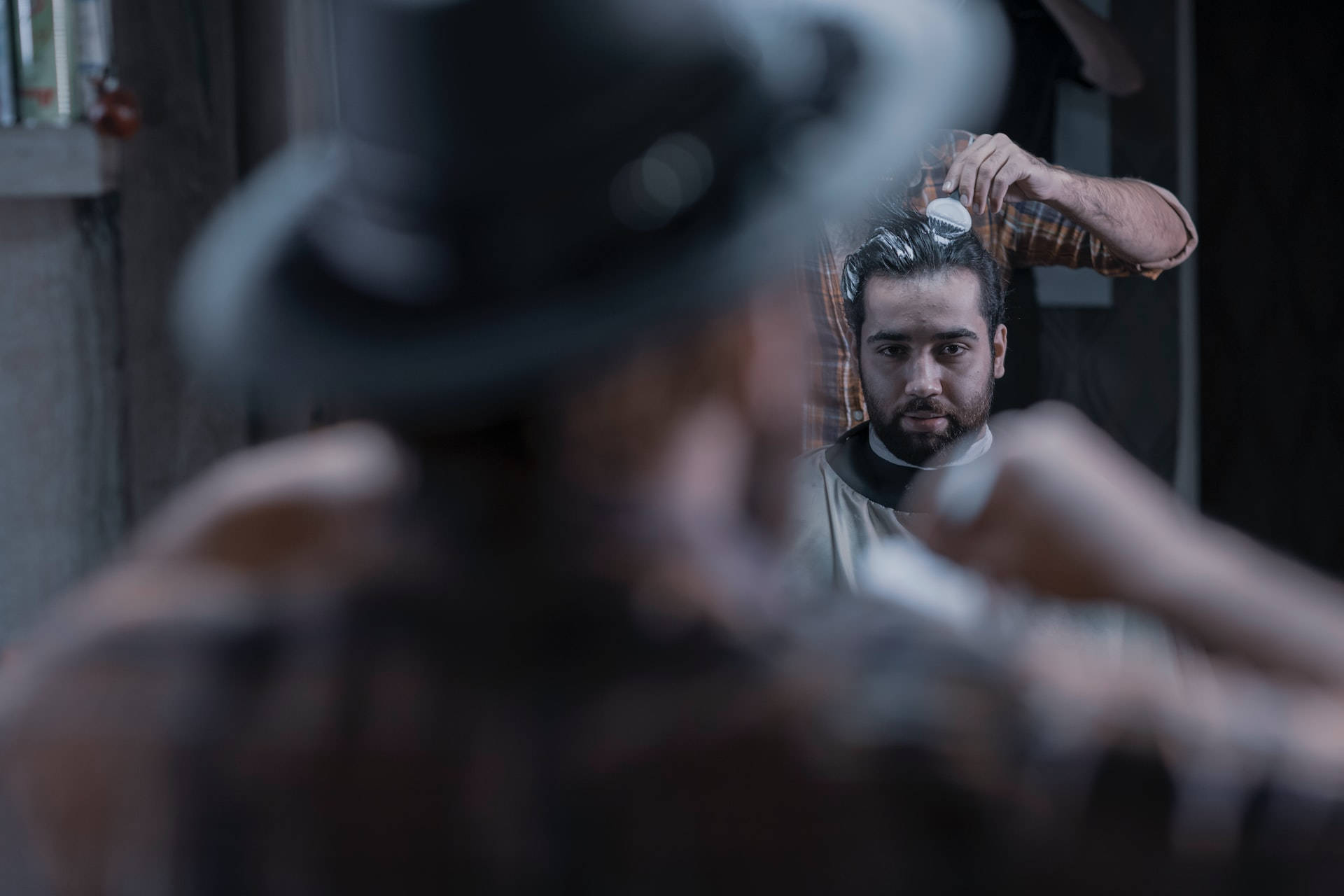 mirror 桌布 壁紙 — 一個留鬍鬚的男人凝視著鏡子，而理髮師在燈光昏暗的理髮店裡為他整理頭髮。