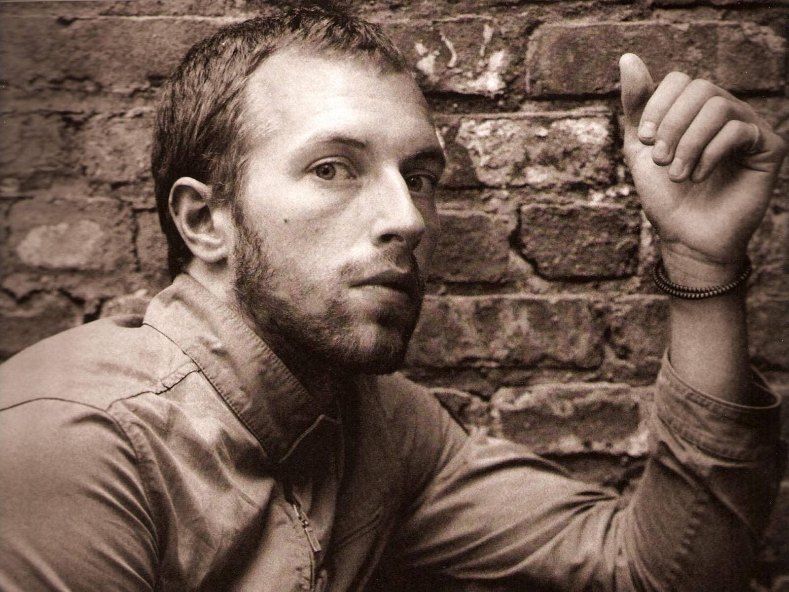 Chris Martin 桌布 壁紙 — 一個留鬍鬚的男人在一張懷舊褐色調的肖像中靠著一幅風化的磚牆。