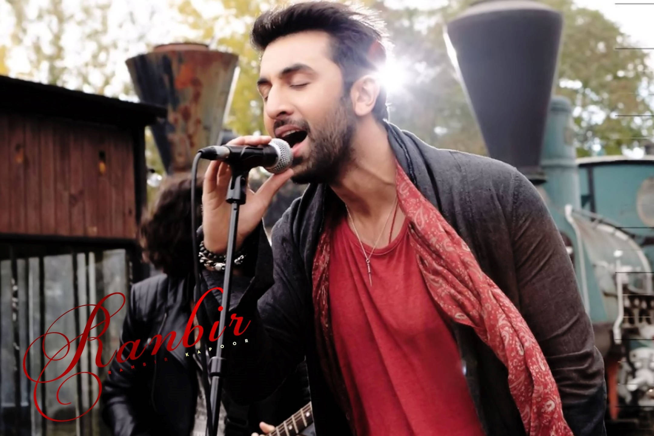 Ranbir Kapoor 桌布 壁紙 — 一個留鬍鬚的男人在戶外熱情地對著麥克風唱歌，背後有陽光。