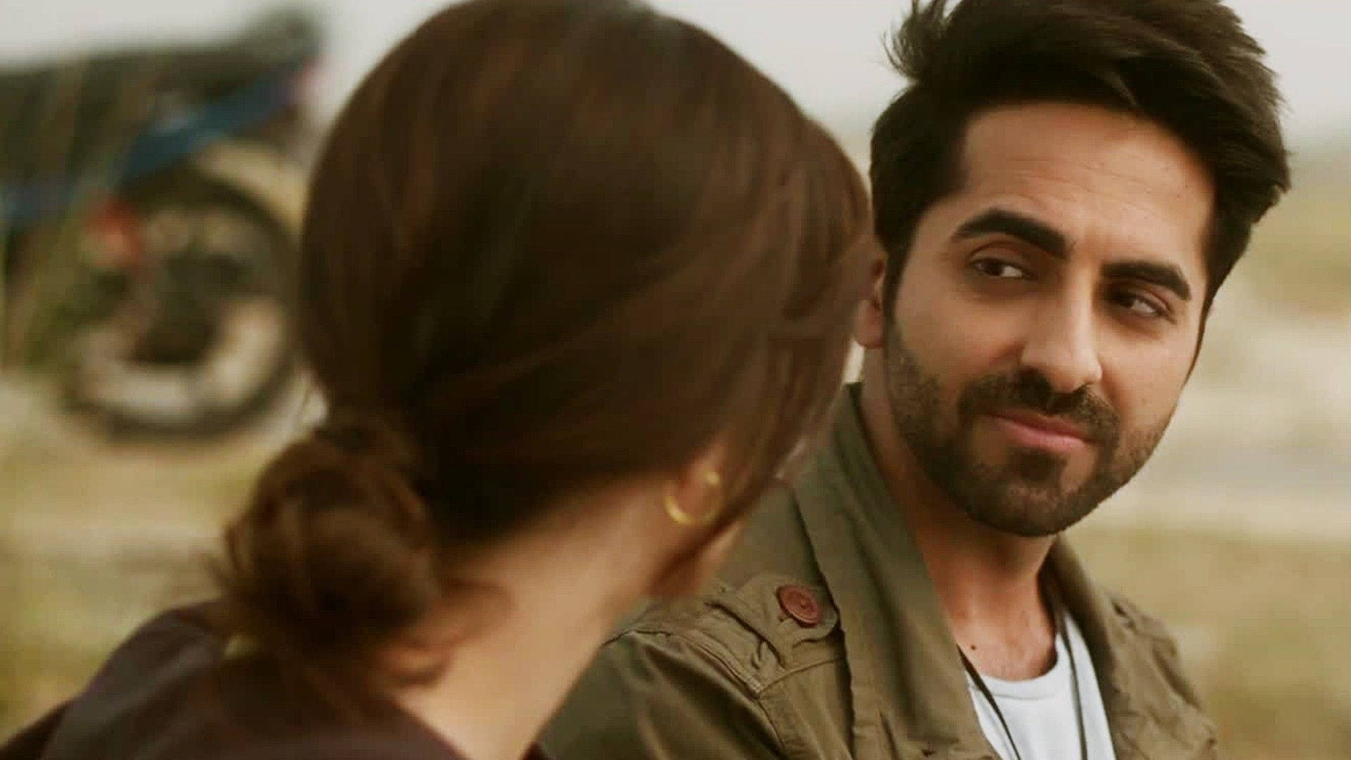 ayushmann khurrana 桌布 壁紙 — 一個留鬍鬚的男人在陽光普照的戶外環境中，專注地凝視著一個背對他的女人。