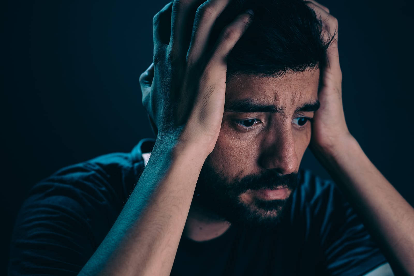 Anxiety 桌布 壁紙 — 一個留鬍鬚的男人在黑暗背景的冷藍色燈光下痛苦地抓住自己的頭。