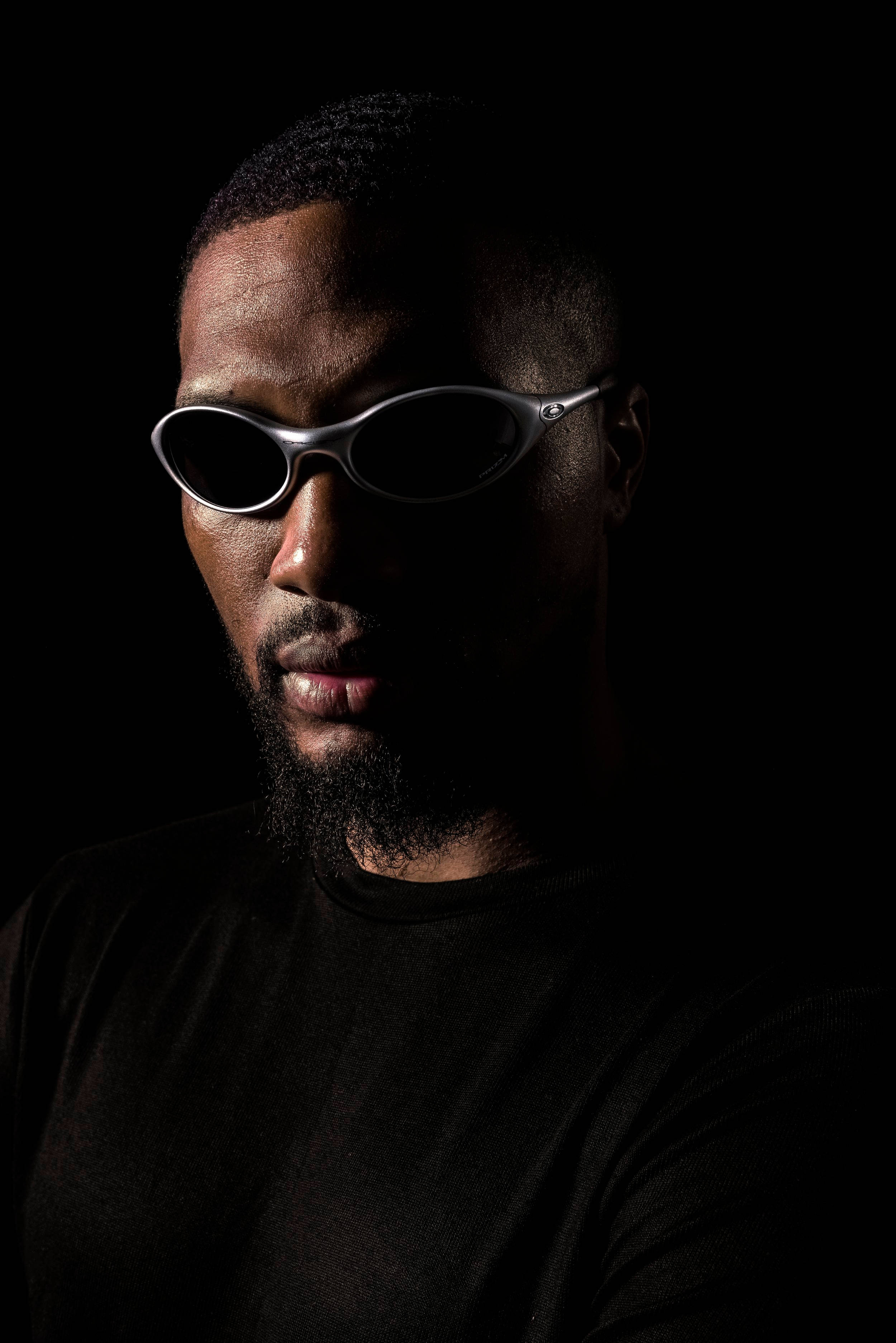 Sunglasses 桌布 壁紙 — 一個留鬍鬚的男人戴著時尚的銀色太陽眼鏡，背景是黑色，側面有強烈的燈光效果。