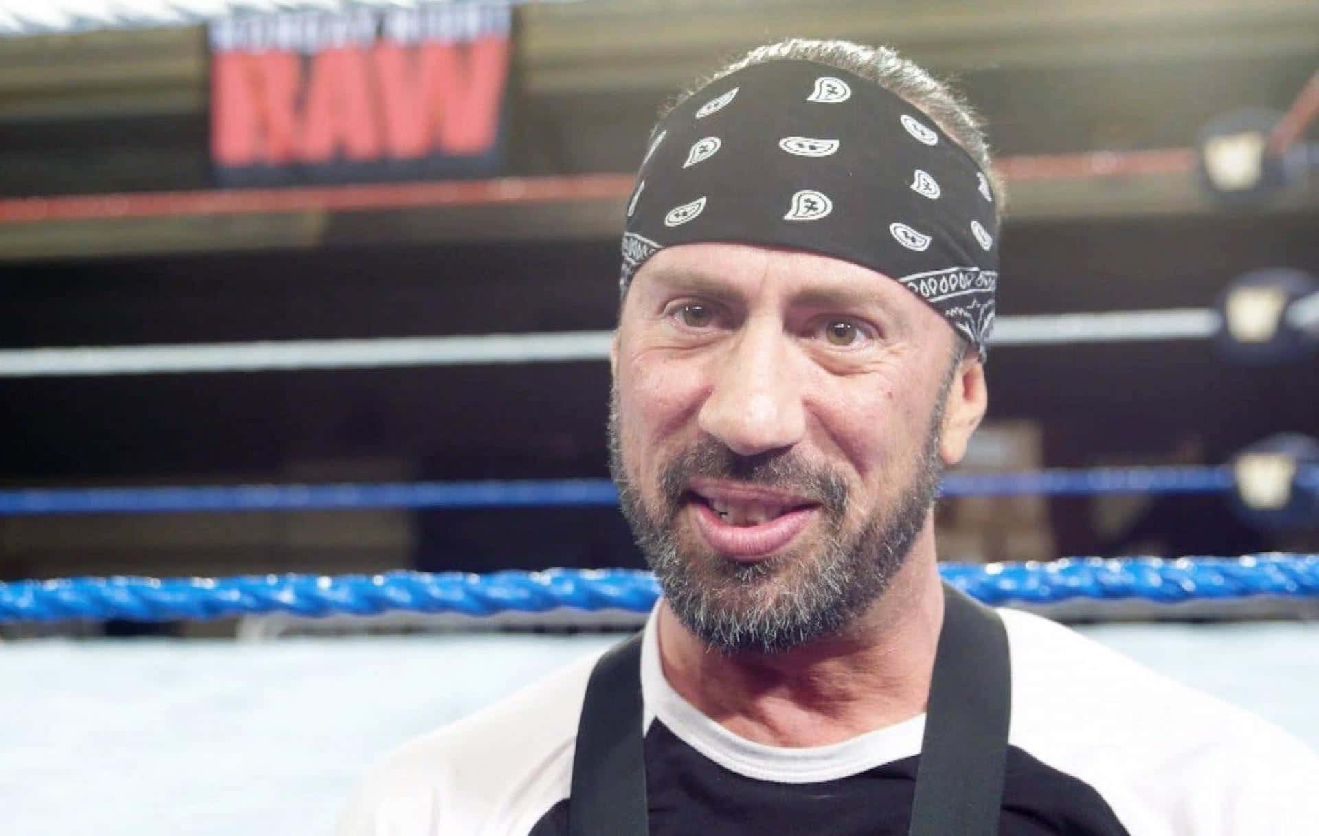 WWE 桌布 壁紙 — 一個留鬍鬚的男人戴著黑色頭巾，在摔角擂台上微笑，身後可見「RAW」標誌。