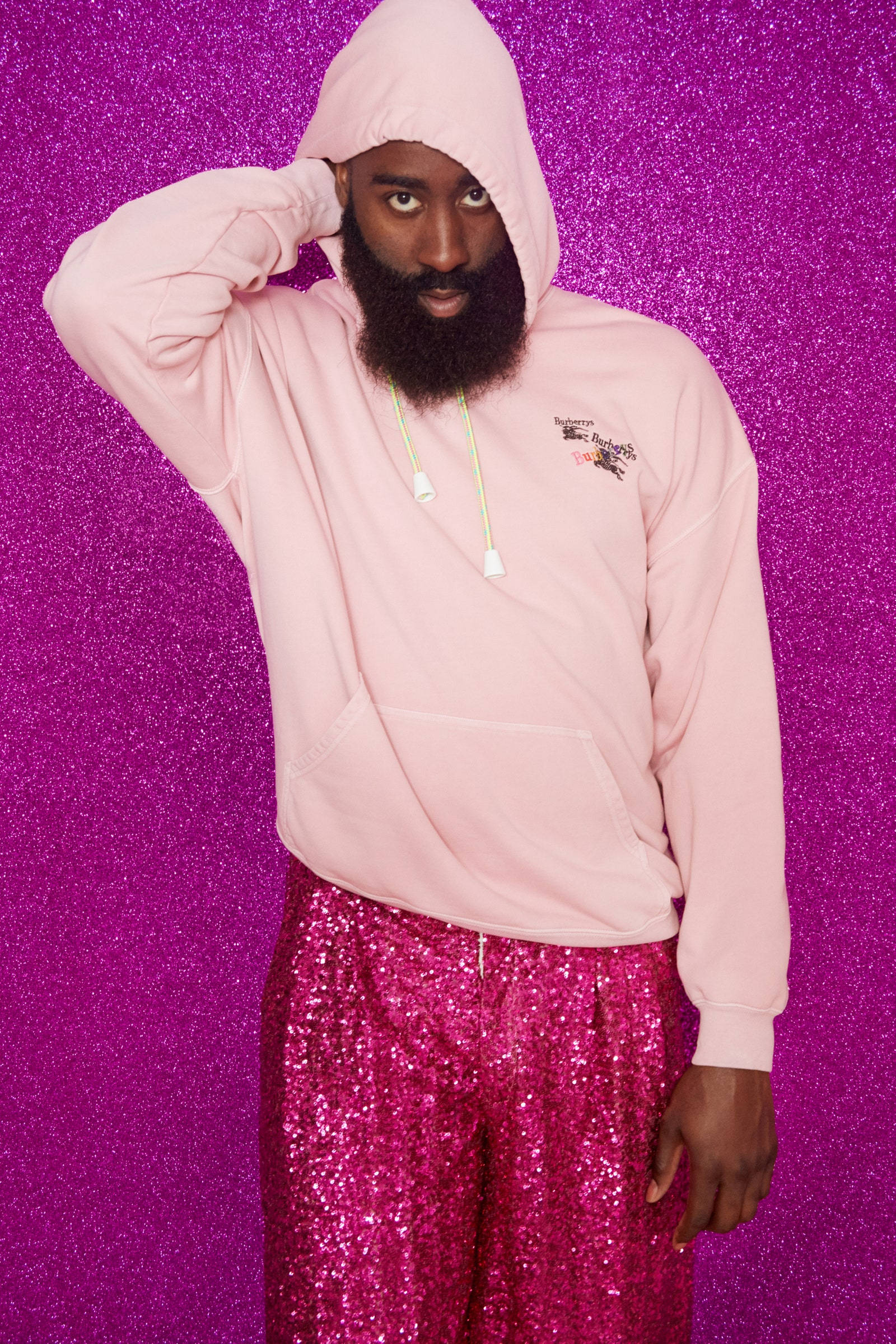James Harden 桌布 壁紙 — 一個留鬍鬚的男人穿著粉紅色連帽衫和閃閃發光的粉紅色褲子，背景是閃爍的紫色。