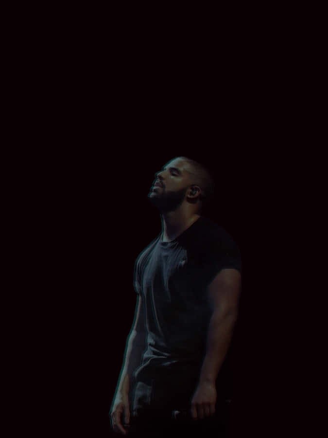 Aesthetic Drake 桌布 壁紙 — 一個留鬍鬚的男人站在近乎黑暗的環境中，他的臉和上半身被上方單一戲劇性的光源照亮。