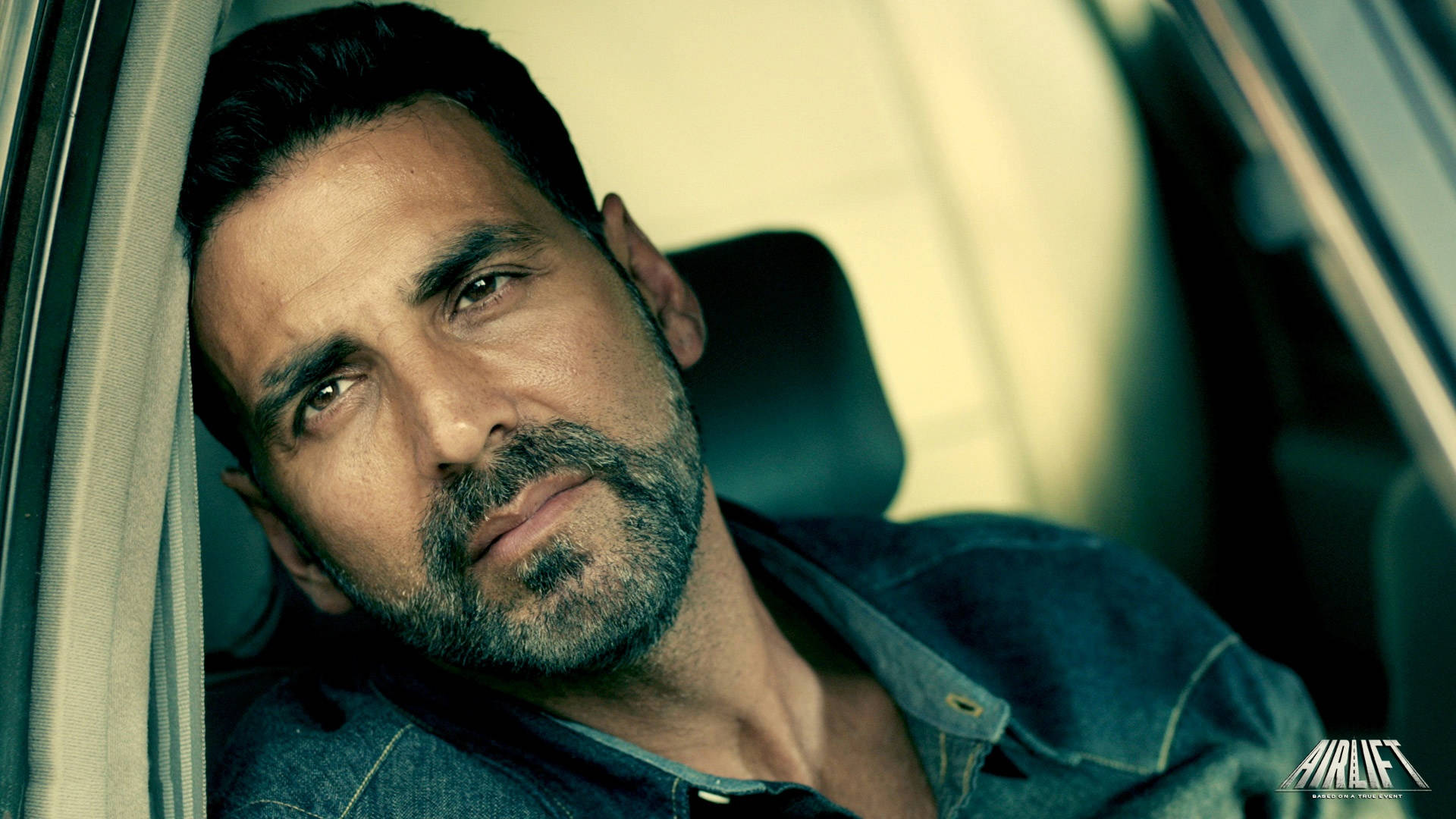 Akshay Kumar 桌布 壁紙 — 一個留鬍鬚的男人靠在車窗，穿著牛仔襯衫，專注地看著鏡頭。