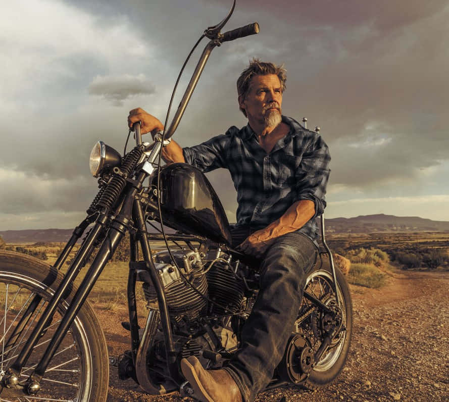 Josh Brolin 桌布 壁紙 — 一個留鬍鬚的粗獷男人坐在黑色chopper機車上，身處廣闊沙漠，天空佈滿戲劇性的雲層。