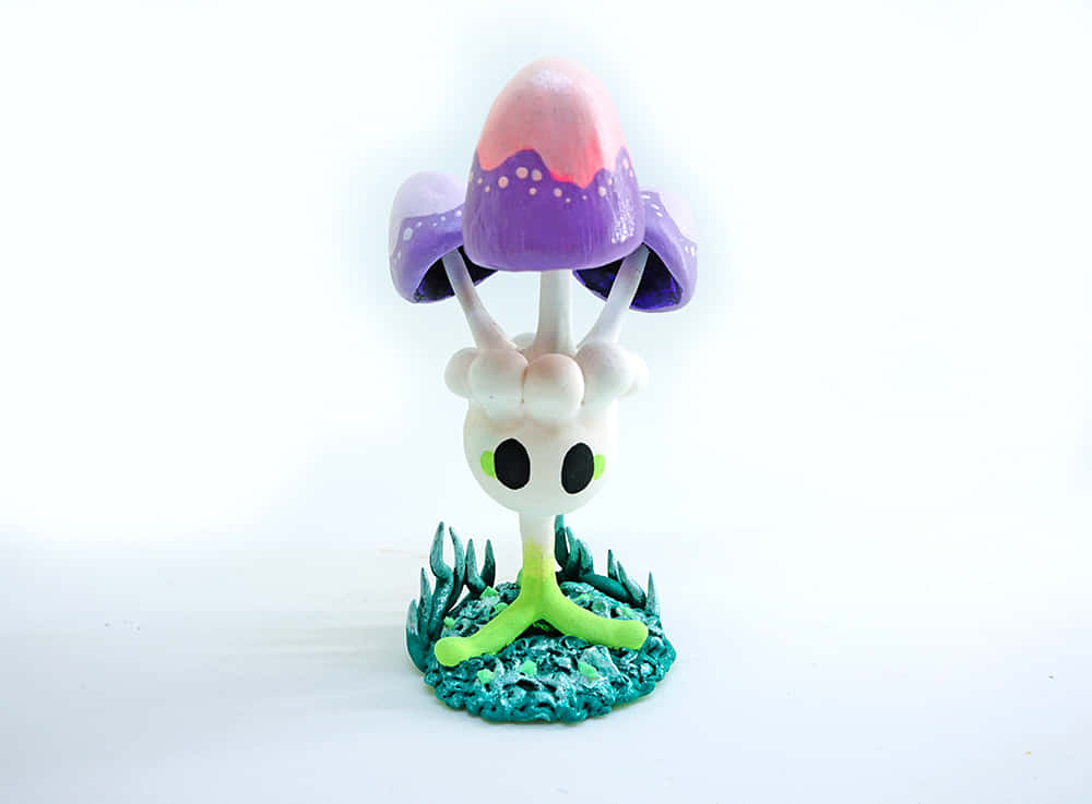 Morelull 桌布 壁紙 — 一個異想天開的手繪蘑菇頭生物公仔，有大大的黑色眼睛和綠色莖，站在有紋理的青綠色底座上，背景是純白色。