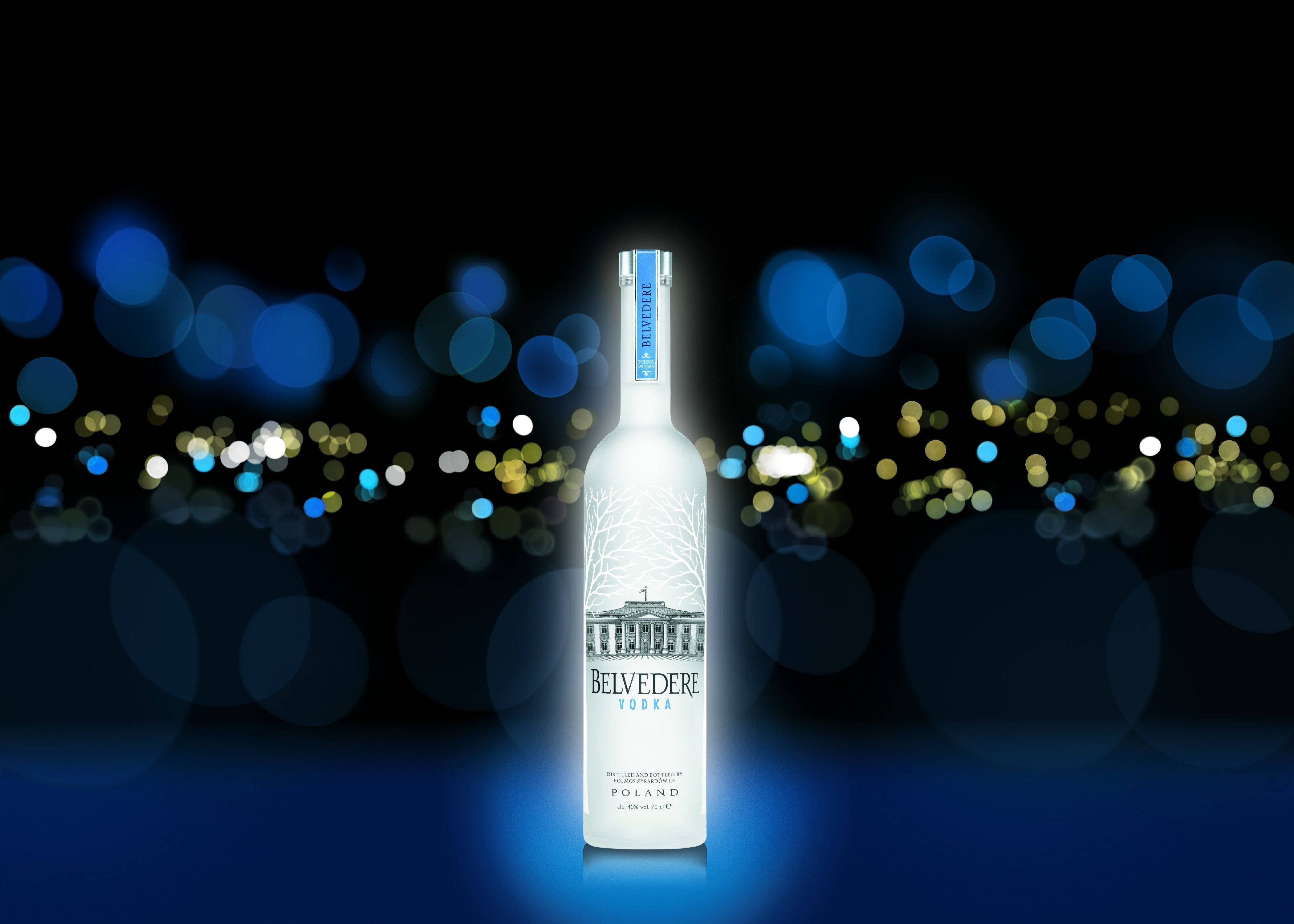 alcohol 桌布 壁紙 — 一個發光的 Belvedere 伏特加酒瓶在藍色和金色散景城市燈光的黑暗背景下居中放置。
