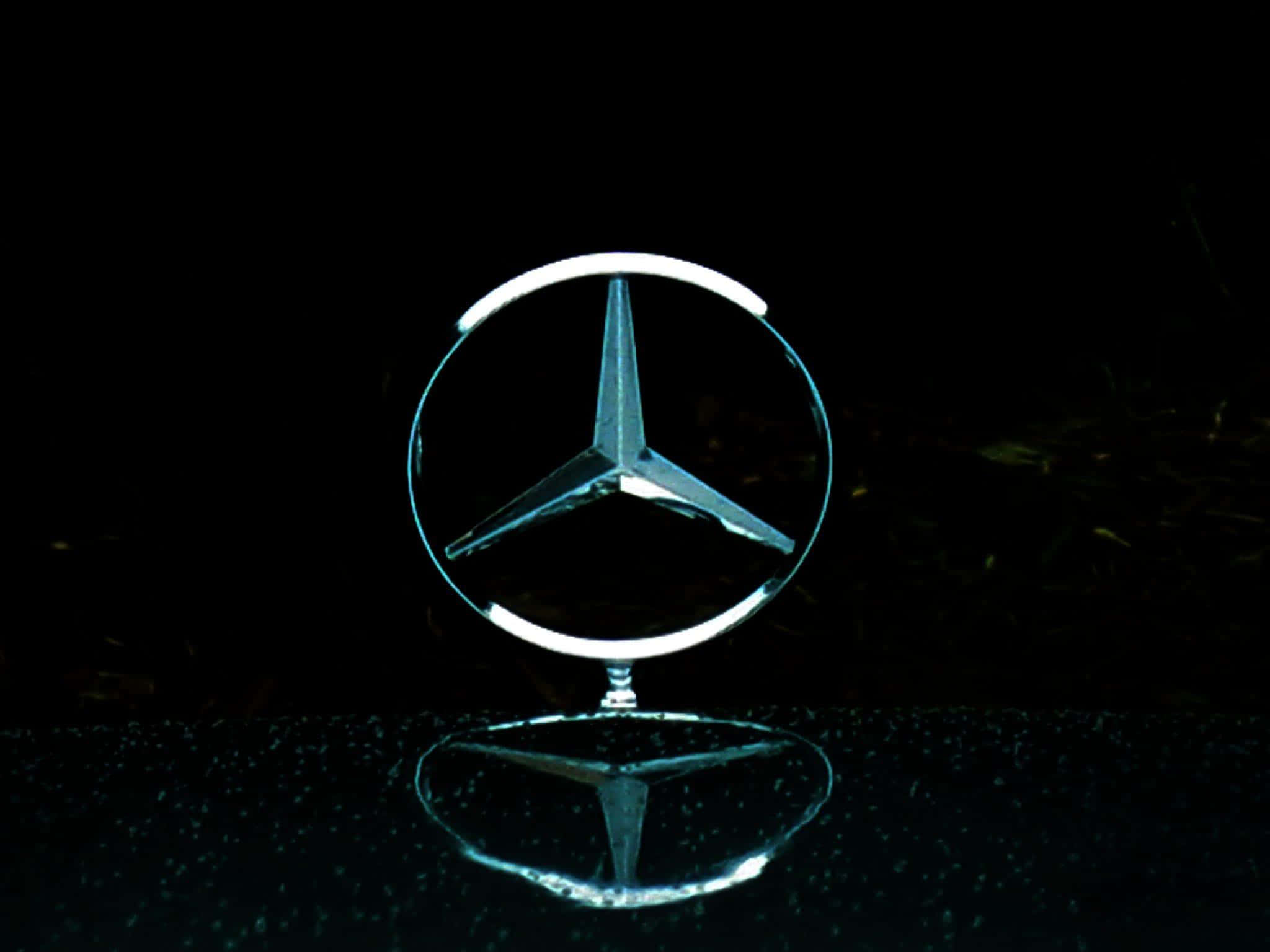 Mercedes Benz Logo 桌布 壁紙 — 一個發光的 Mercedes-Benz 標誌置中於反射表面上，背景為純黑色。