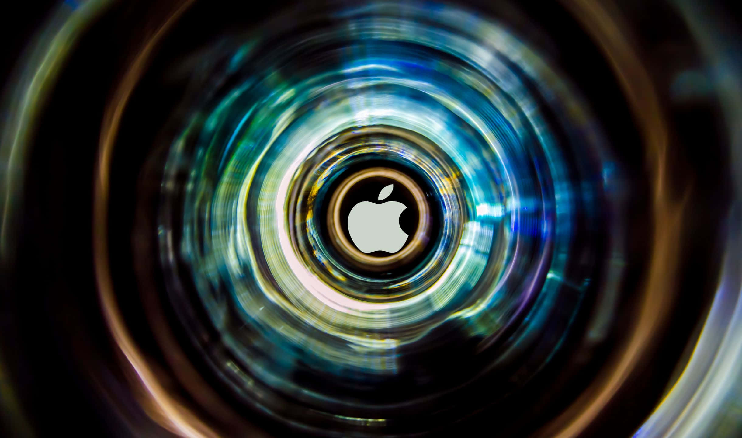 2440x1440 Apple 桌布 壁紙 — 一個發光的Apple標誌，位於充滿活力的藍色和金色光線漩渦隧道中央。