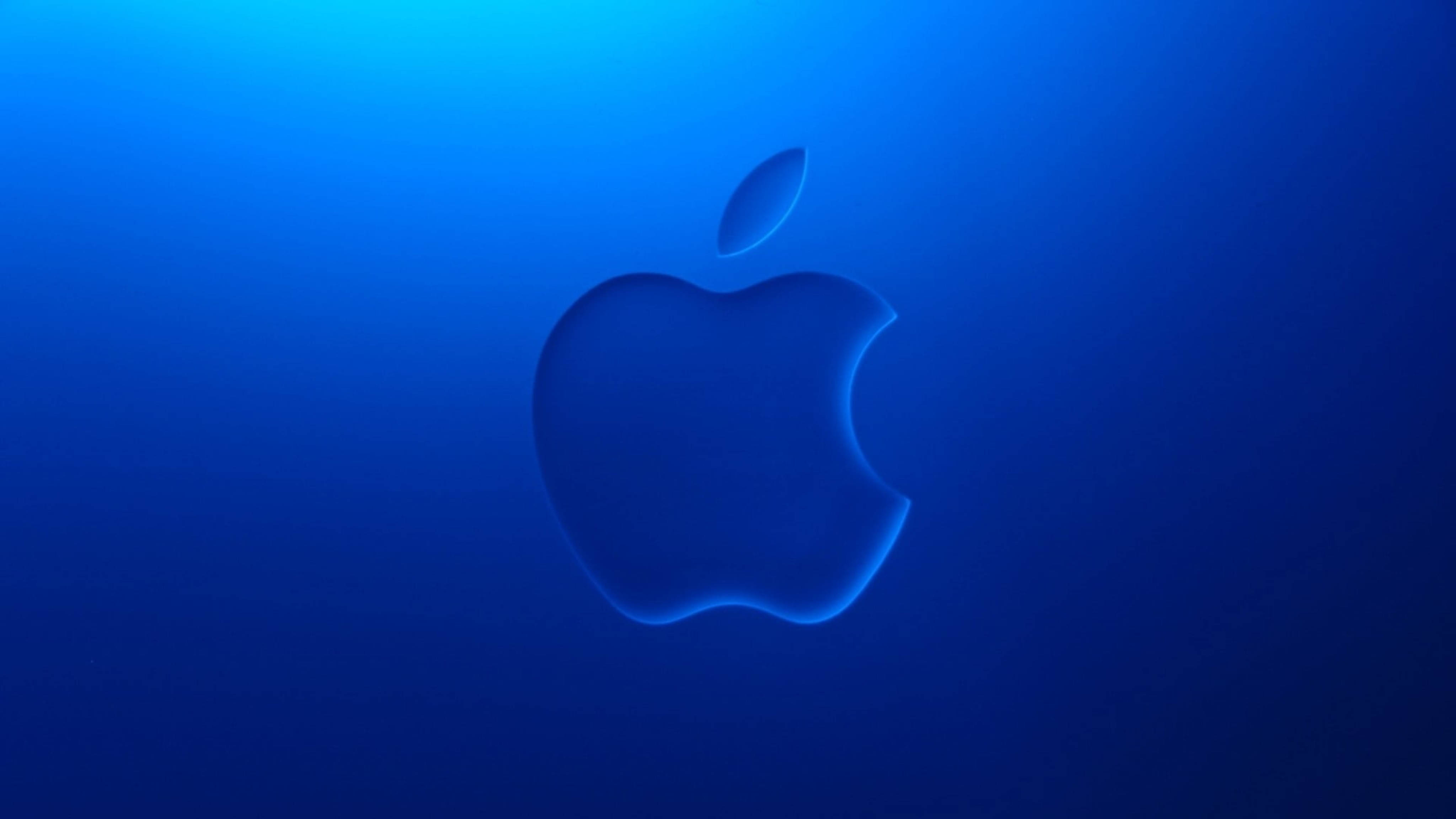 Apple 4K Ultra HD 桌布 壁紙 — 一個發光的Apple標誌漂浮在漸變藍色背景上，柔和的光線從上方照射。