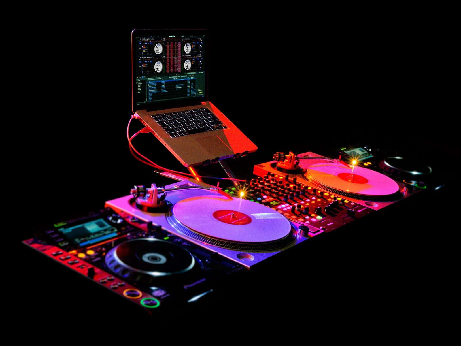 vinyl 桌布 壁紙 — 一個發光的DJ設備，有兩個唱盤和一部筆記型電腦，浸沒在霓虹粉紅和紫色燈光中，背景為黑色。
