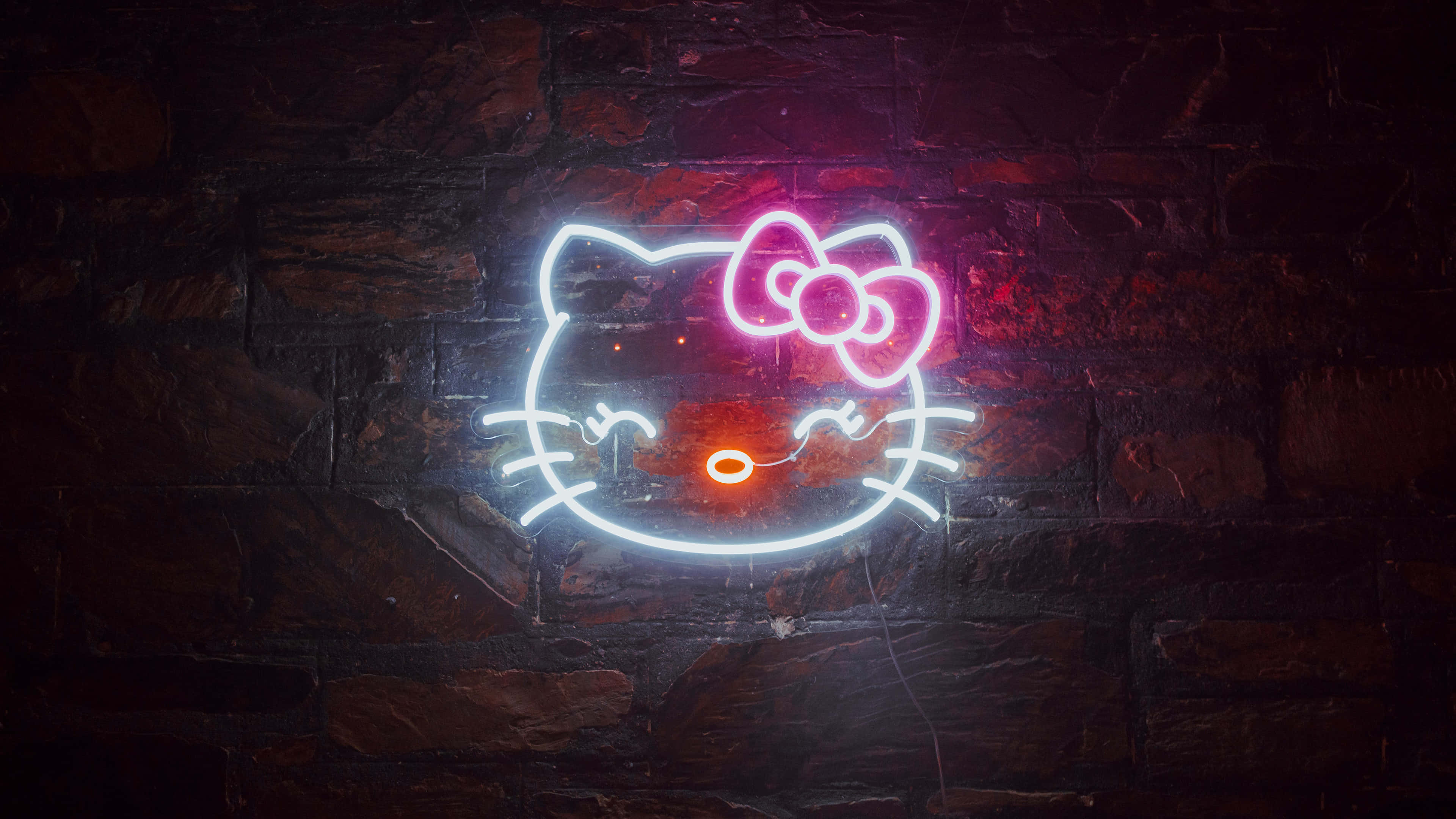 neon sign 桌布 壁紙 — 一個發光的Hello Kitty霓虹燈牌，帶有粉紅色蝴蝶結和橙色鼻子，在深色磚牆上投射出鮮豔的光芒。