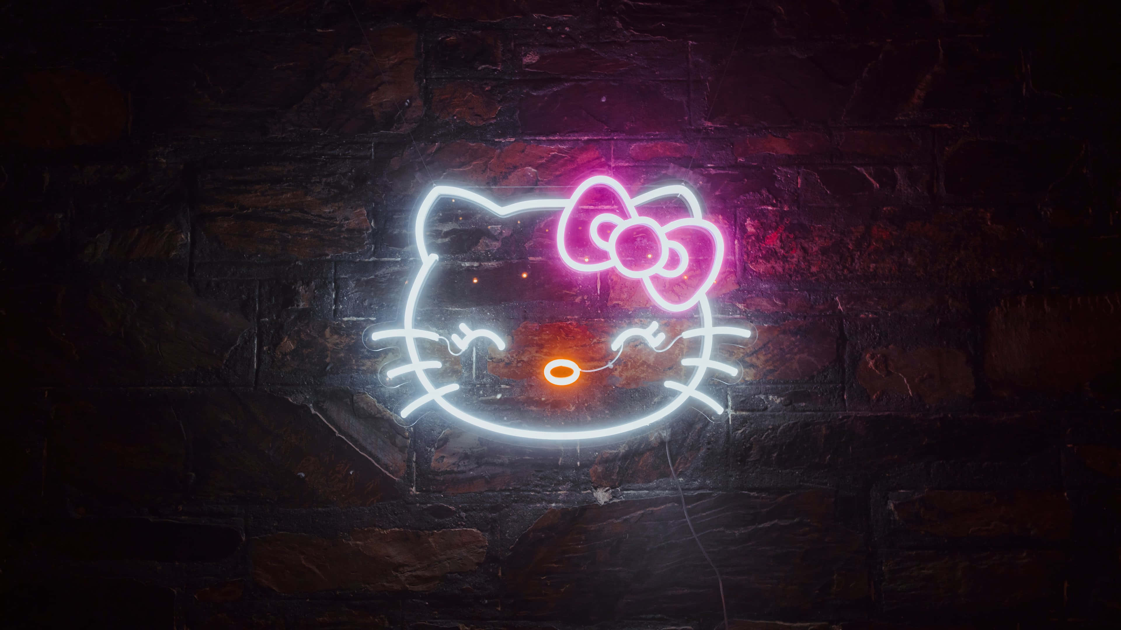 Hello Kitty Pc 桌布 壁紙 — 一個發光的Hello Kitty霓虹燈牌，帶有粉紅色蝴蝶結和橙色鼻子，在夜間照亮了深色磚牆。