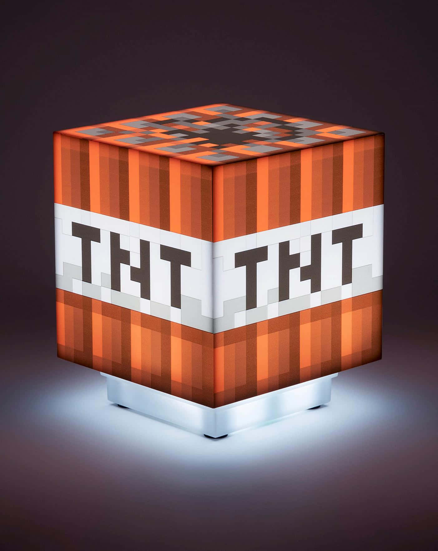 遊戲 桌布 壁紙 — 一個發光的Minecraft TNT方塊燈，帶有像素化的橙色條紋和粗體黑色文字，在黑暗表面上投射柔和光線。